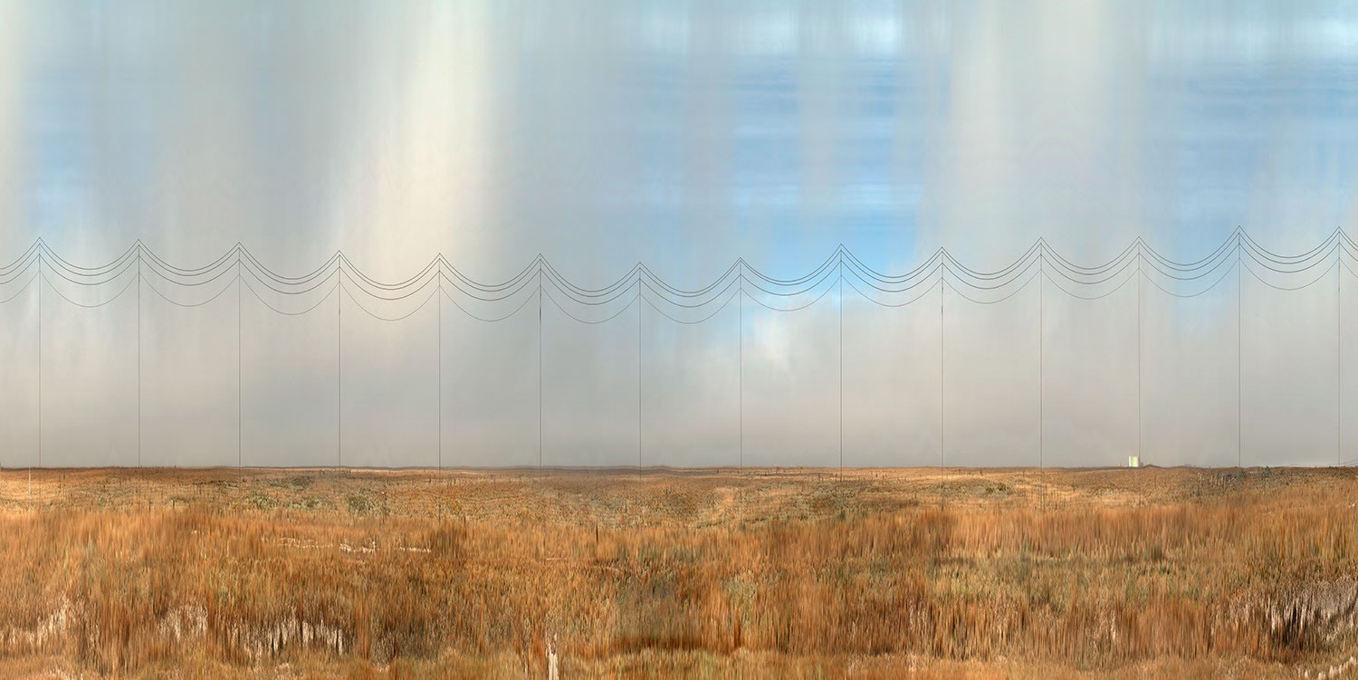 A wide landscape with flat terrain and dry, grassy fields. Multiple tall, thin poles connected by curved wires extend across the horizon under a cloudy sky—the scenery reminiscent of Ansen Seale’s work in The Transient Landscape.