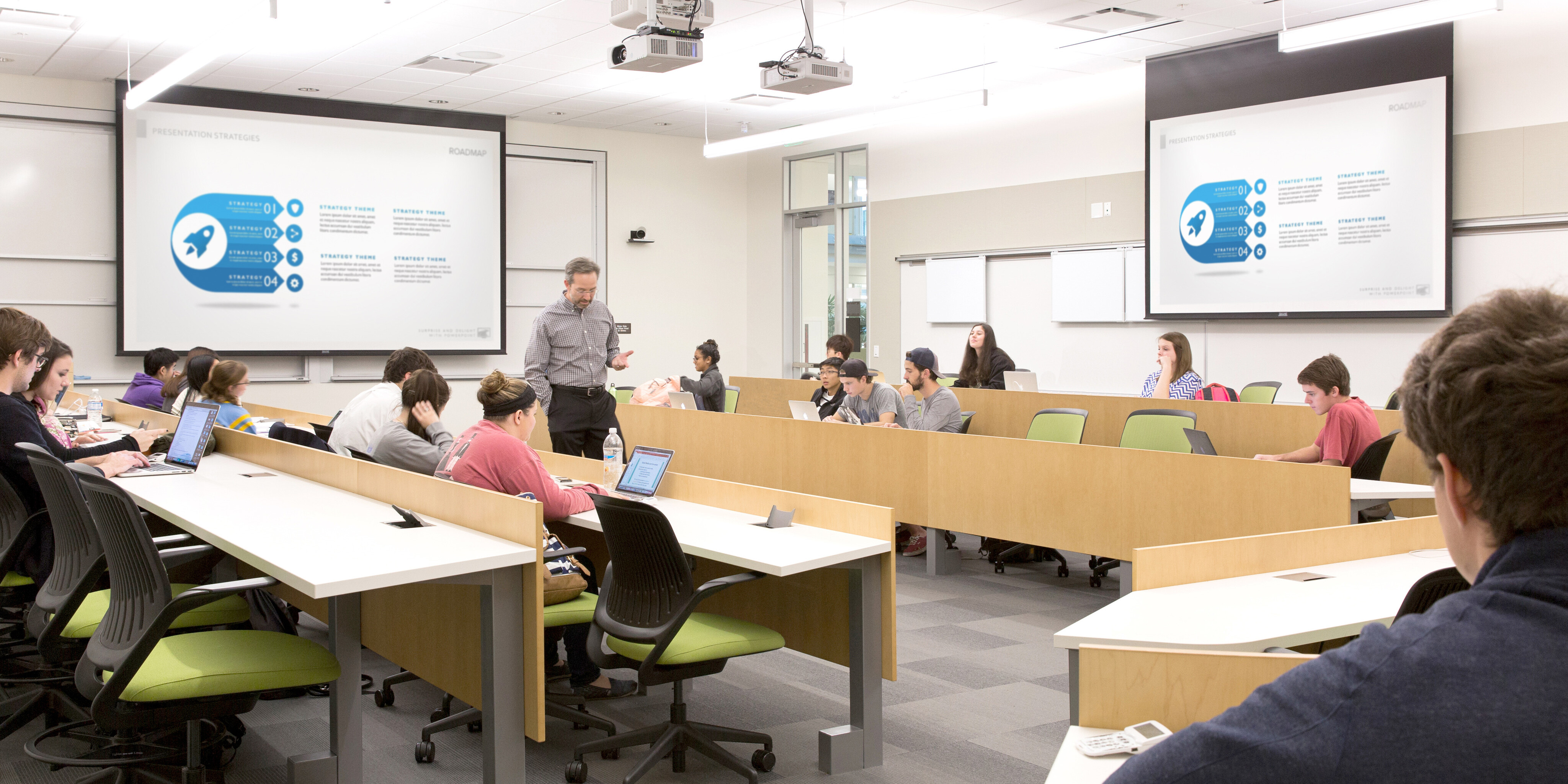 A classroom within the Baylor School of Business features students seated at desks, some using laptops. A teacher stands in front, presenting a slide on "Product Strategy Roadmap" displayed on a screen.