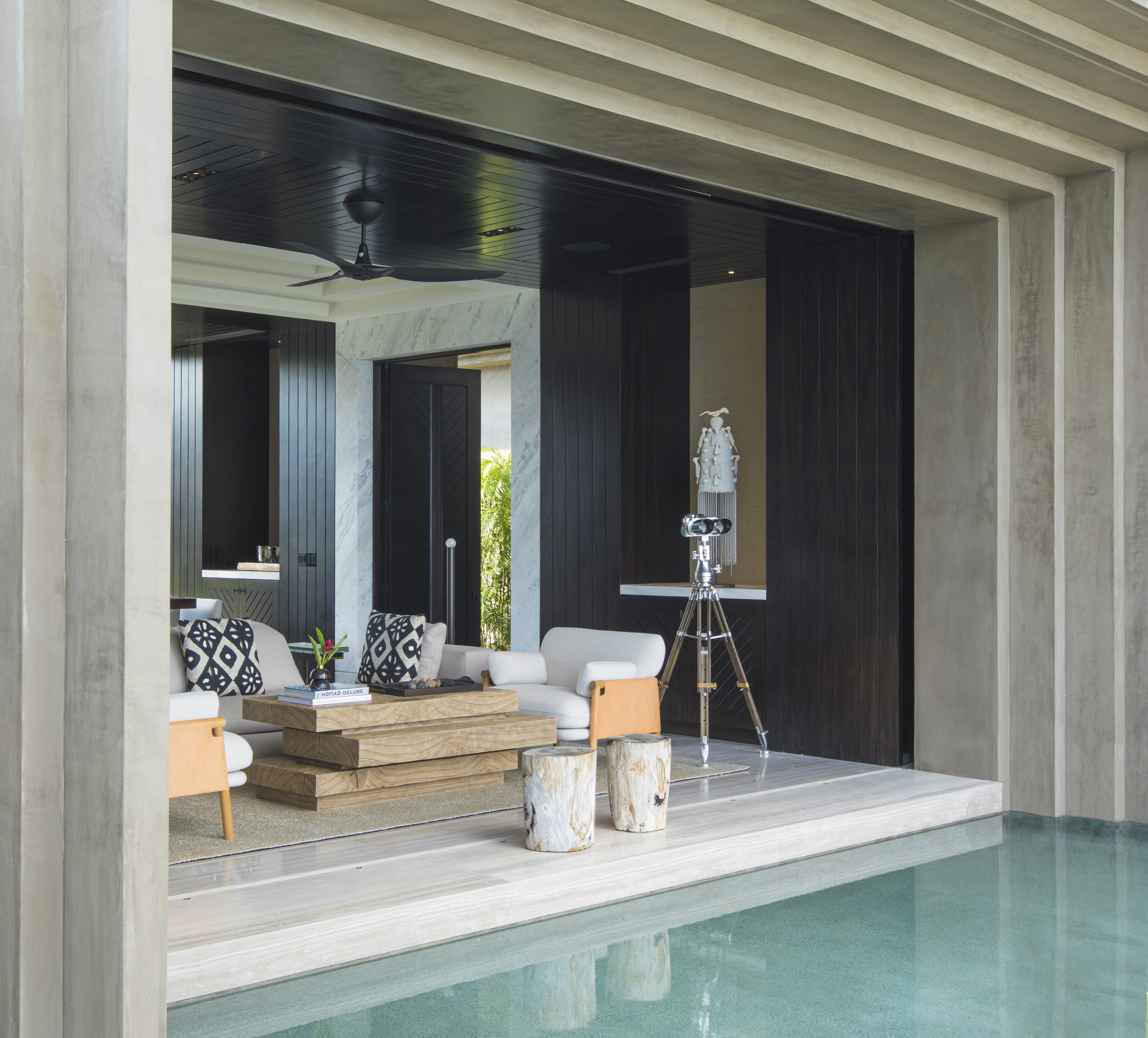 A modern, open-concept living room with light-colored furniture, a wooden coffee table, black walls, a telescope, and an open view of La Cascada's concrete patio with glossy green flooring.