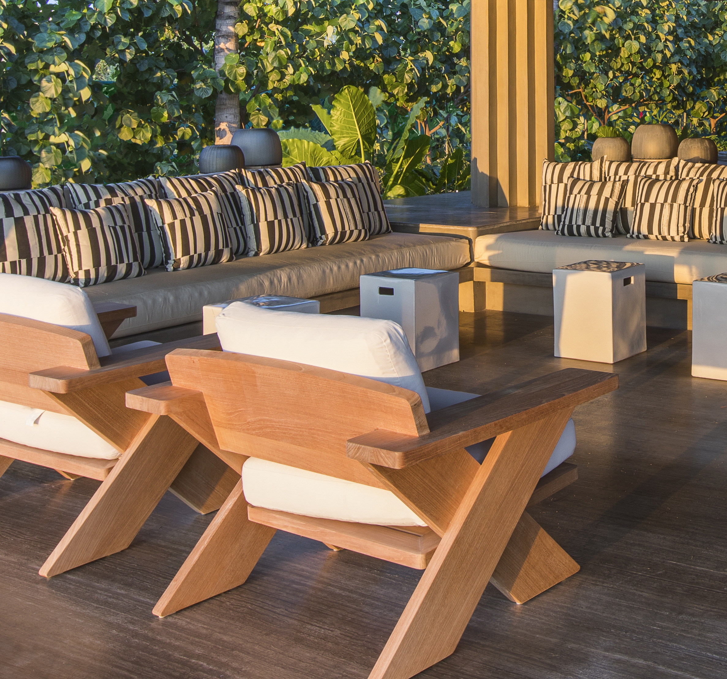 La Cascada's outdoor seating area features wooden chairs and cushioned sofas arranged around small tables on a wooden deck, surrounded by lush greenery.