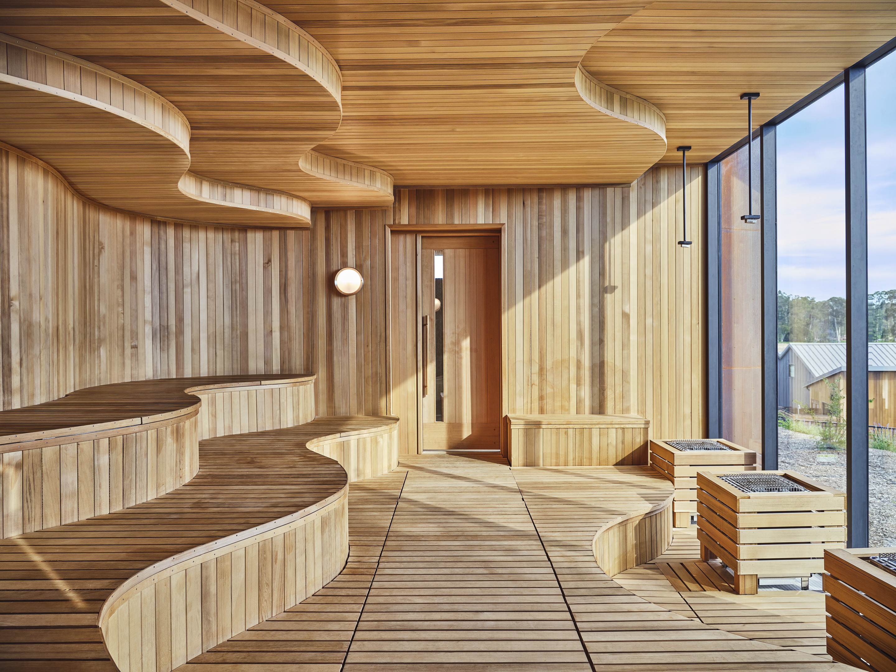 Modern wooden sauna interior with tiered curved seating and a large window facing outside, reminiscent of the luxurious designs found in Auberge Resorts Collection at Stanly Ranch.