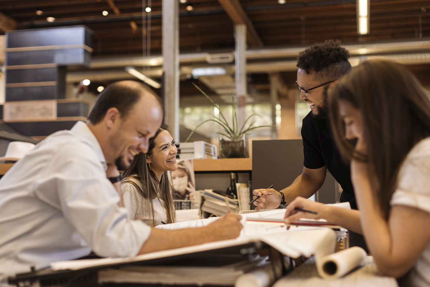 A group of four people sit at a table in an office, engaged in discussion and smiling while looking at documents.