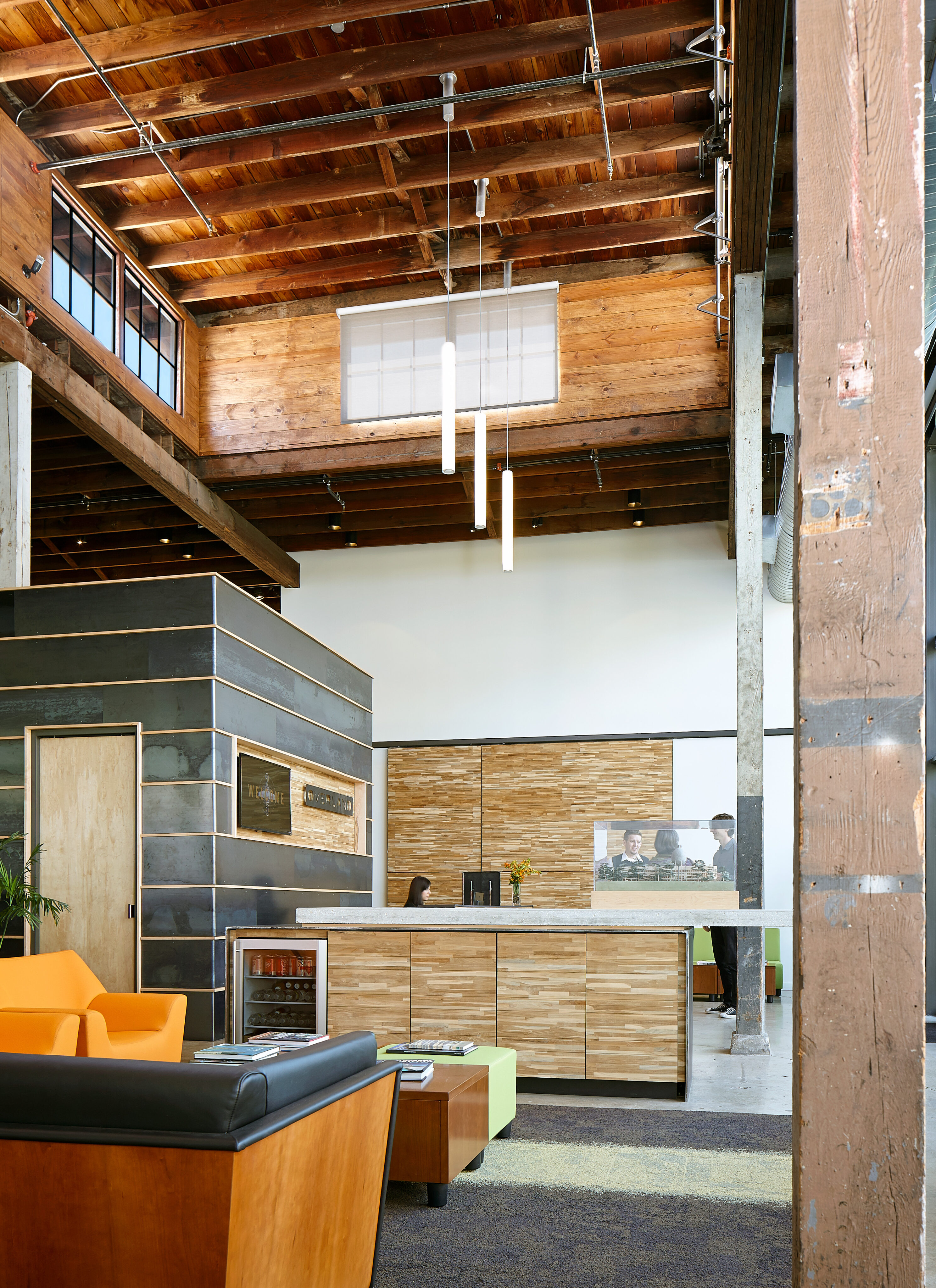 Modern office lobby at Overland HQ featuring wooden accents, a reception desk, seating area with orange and wooden chairs, and high ceilings with exposed beams.