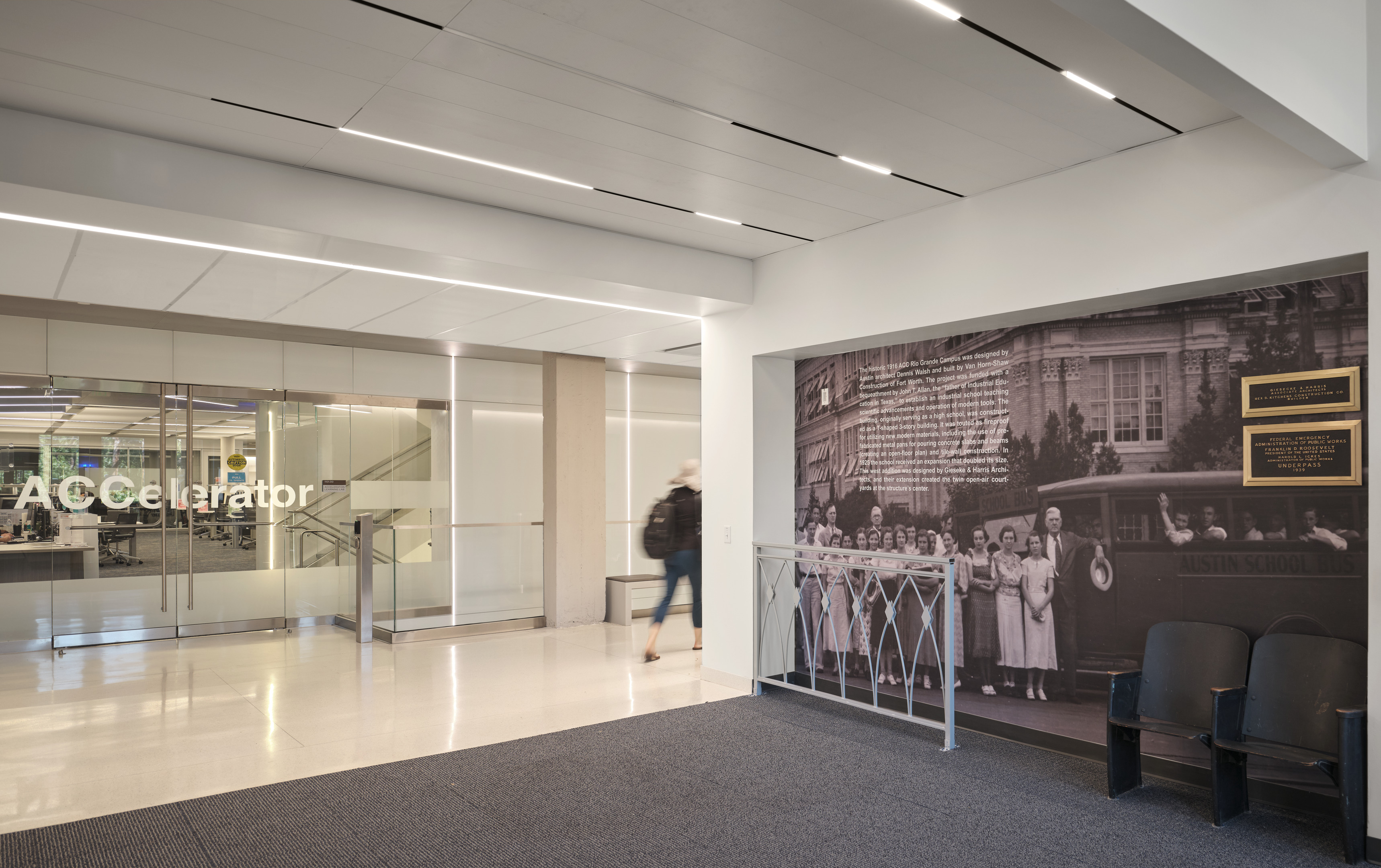 A modern hallway at Austin Community College features glass doors labeled "ACCelerator" on the left and a historical photo mural of the Rio Grande on the right. A person walks through the space, with two chairs in the bottom right corner, showcasing a seamless blend of history and contemporary design.