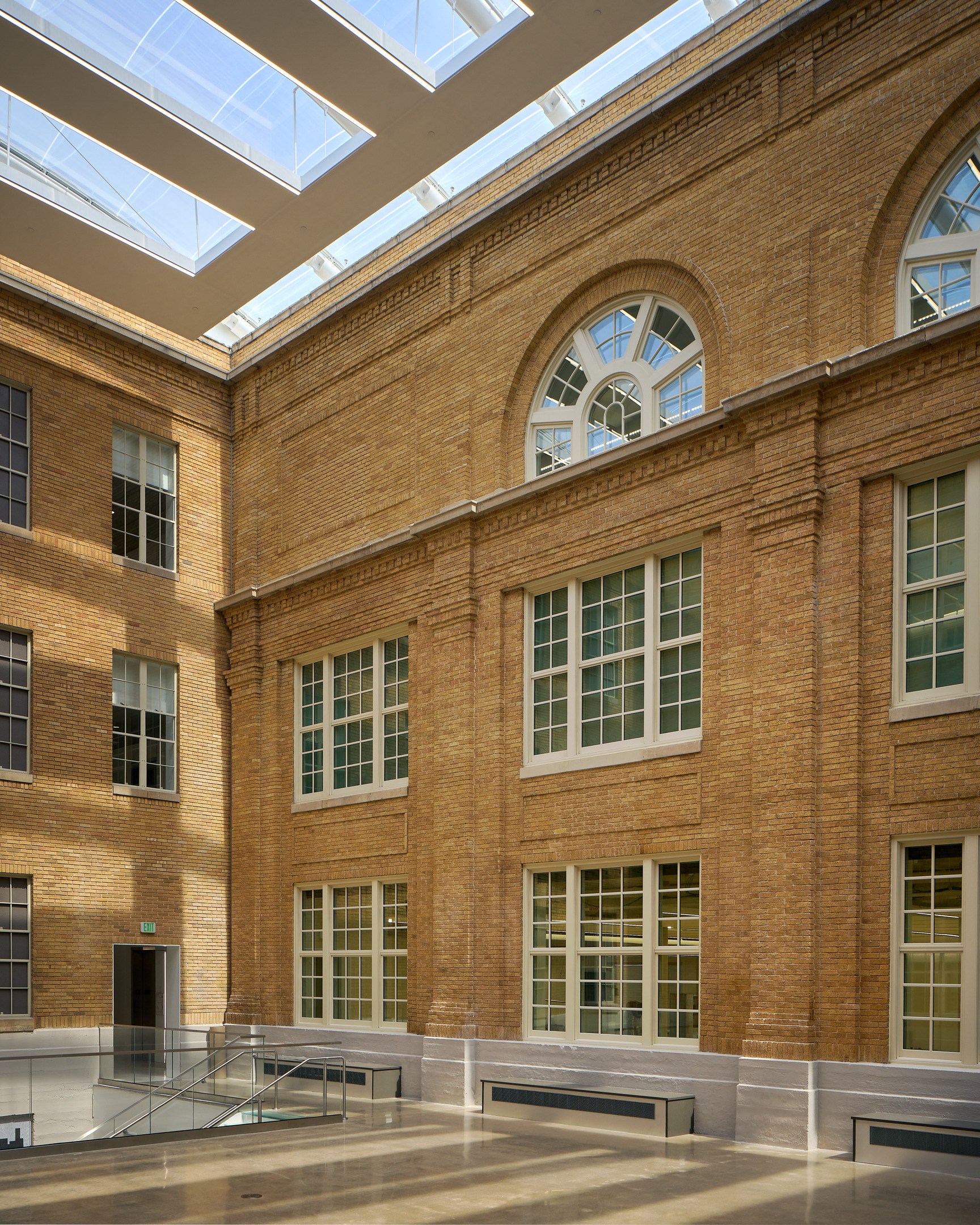 Interior view of a spacious atrium at Austin Community College, featuring brick walls, large windows, and a skylight ceiling allowing natural light to flood the area—a recent renovation that perfectly blends modern design with classic elements.