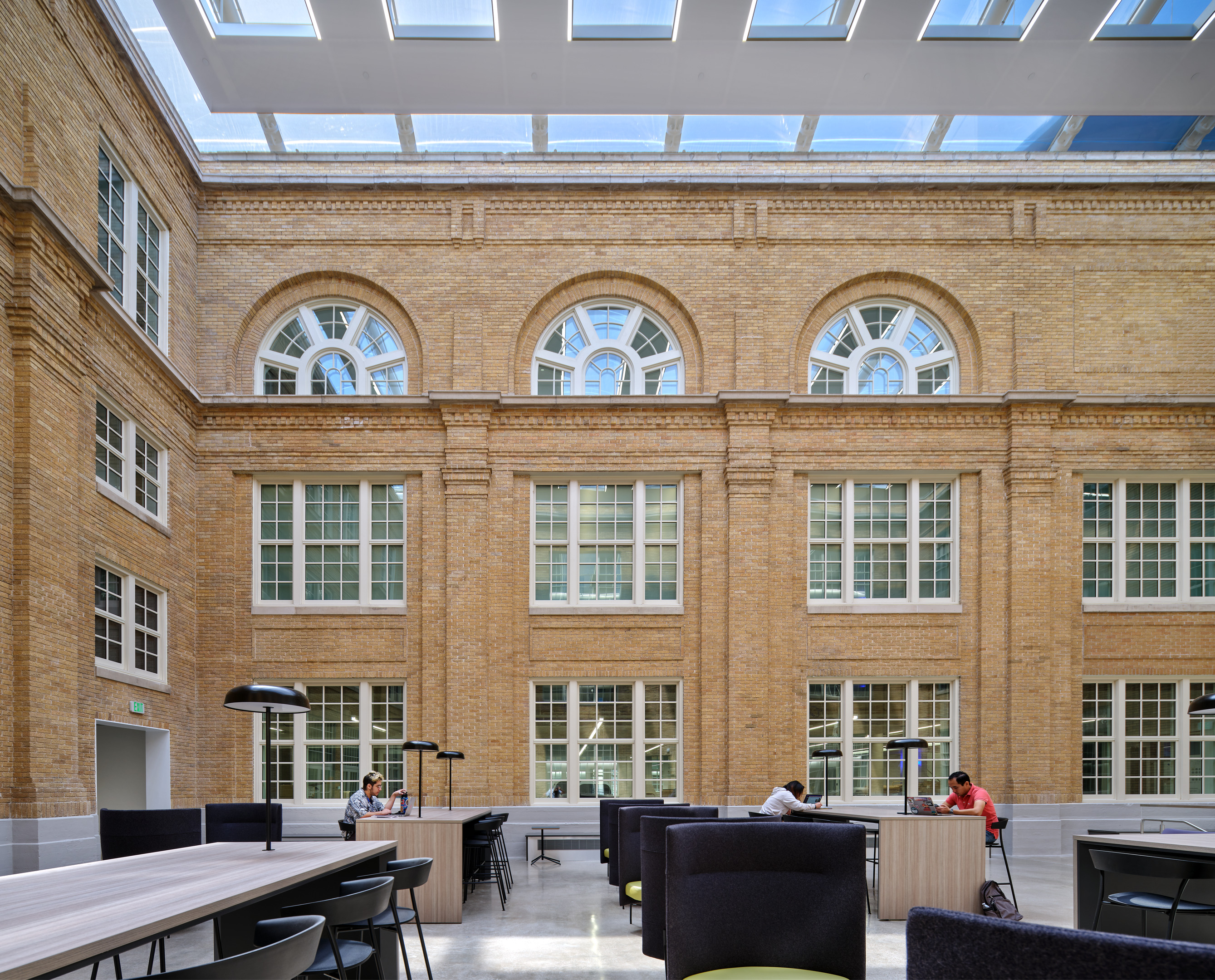 A spacious, modern atrium at Austin Community College's Rio Grande campus features large arched windows, skylights, and people seated at tables working and conversing.