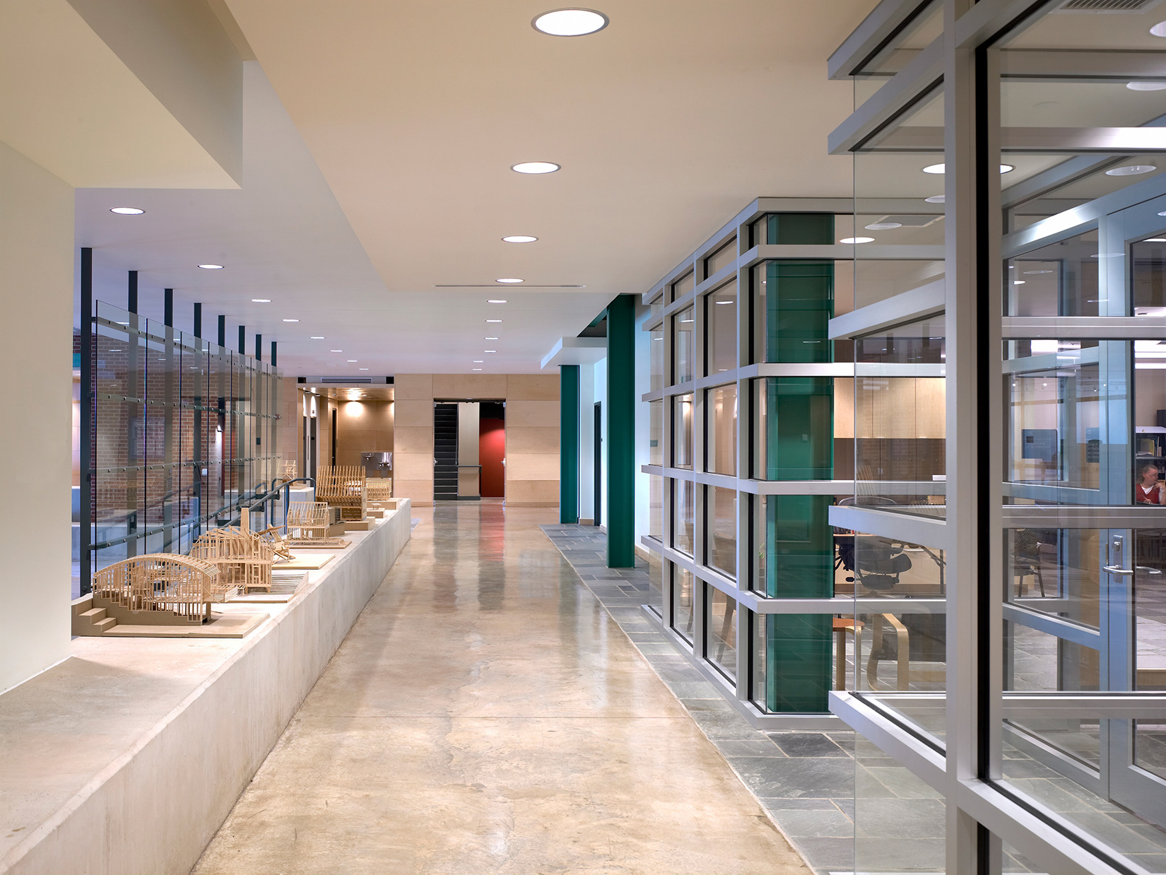 Modern interior hallway with polished concrete floors, large windows, and wicker chairs along one side. The space, reminiscent of the contemporary elegance seen in Penn State's SOA buildings, is well-lit with ceiling lights and an abundance of natural light.