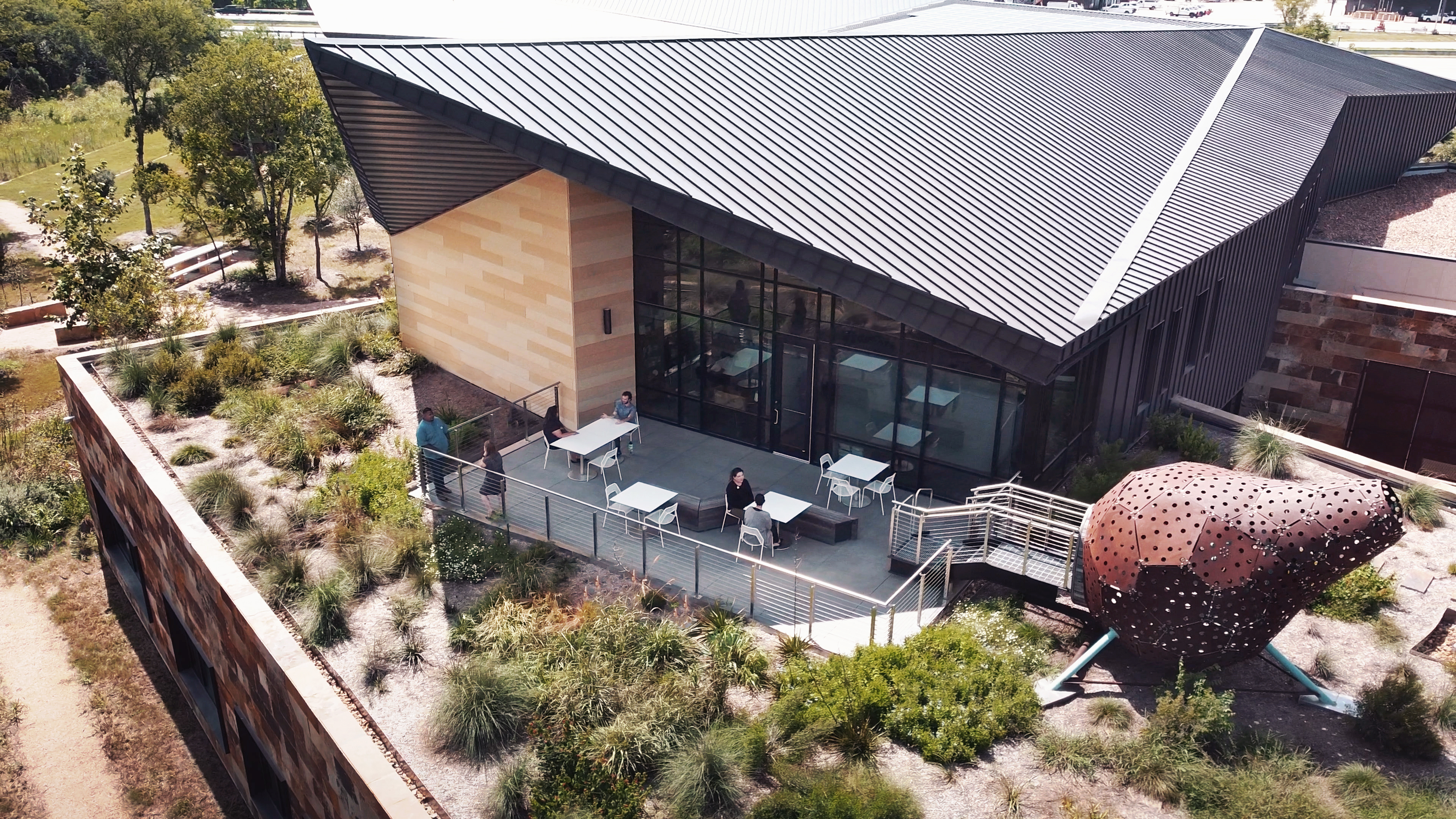 Aerial view of the Harvey E. Najim Children & Family Center with a rooftop garden, outdoor seating area, and unique architectural design. Several people are seated at tables, enjoying the serene atmosphere.