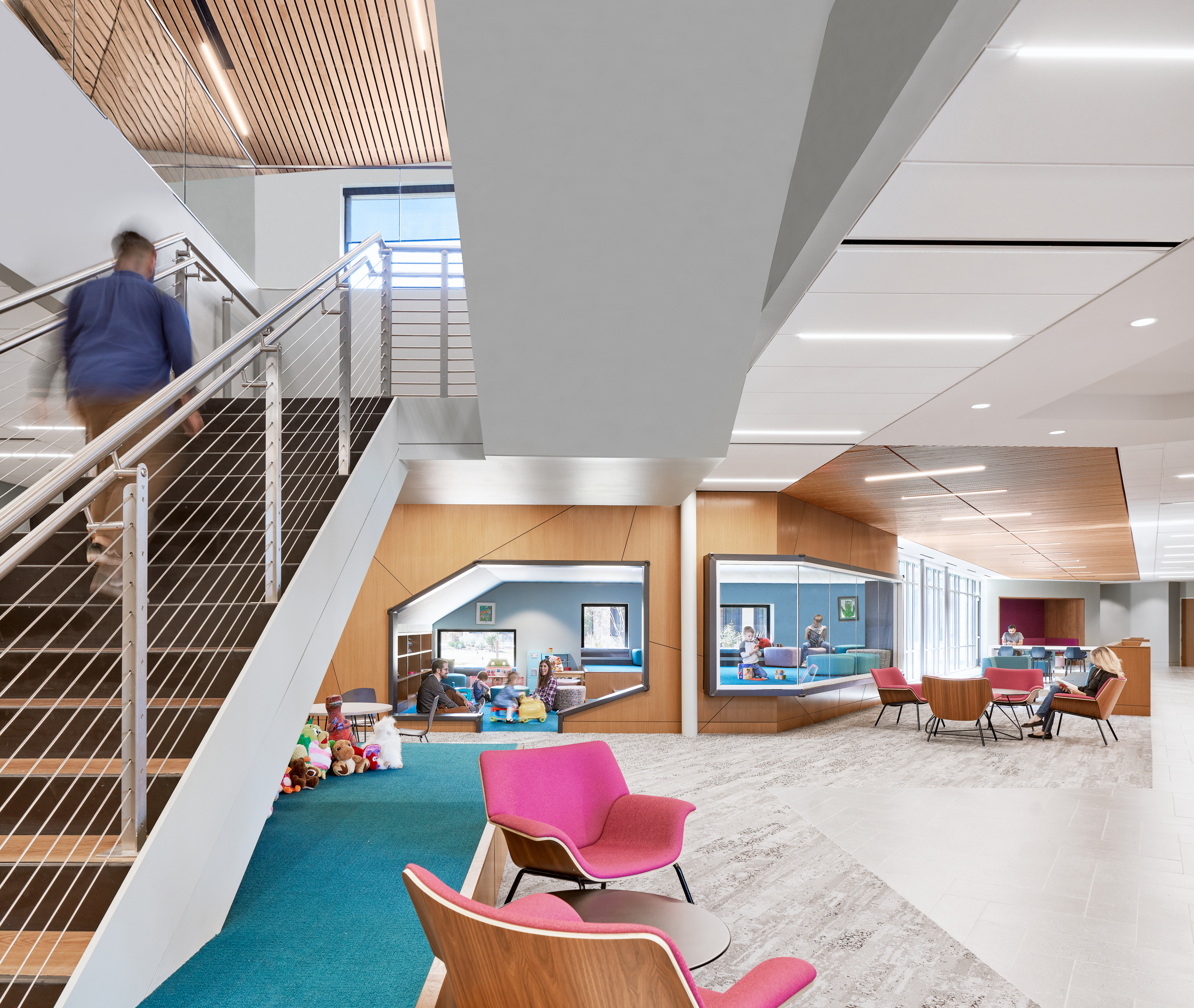 A modern, open office space with a staircase to the left, colorful furniture, a play area at Harvey E. Najim Children & Family Center, and people working and interacting in the background.