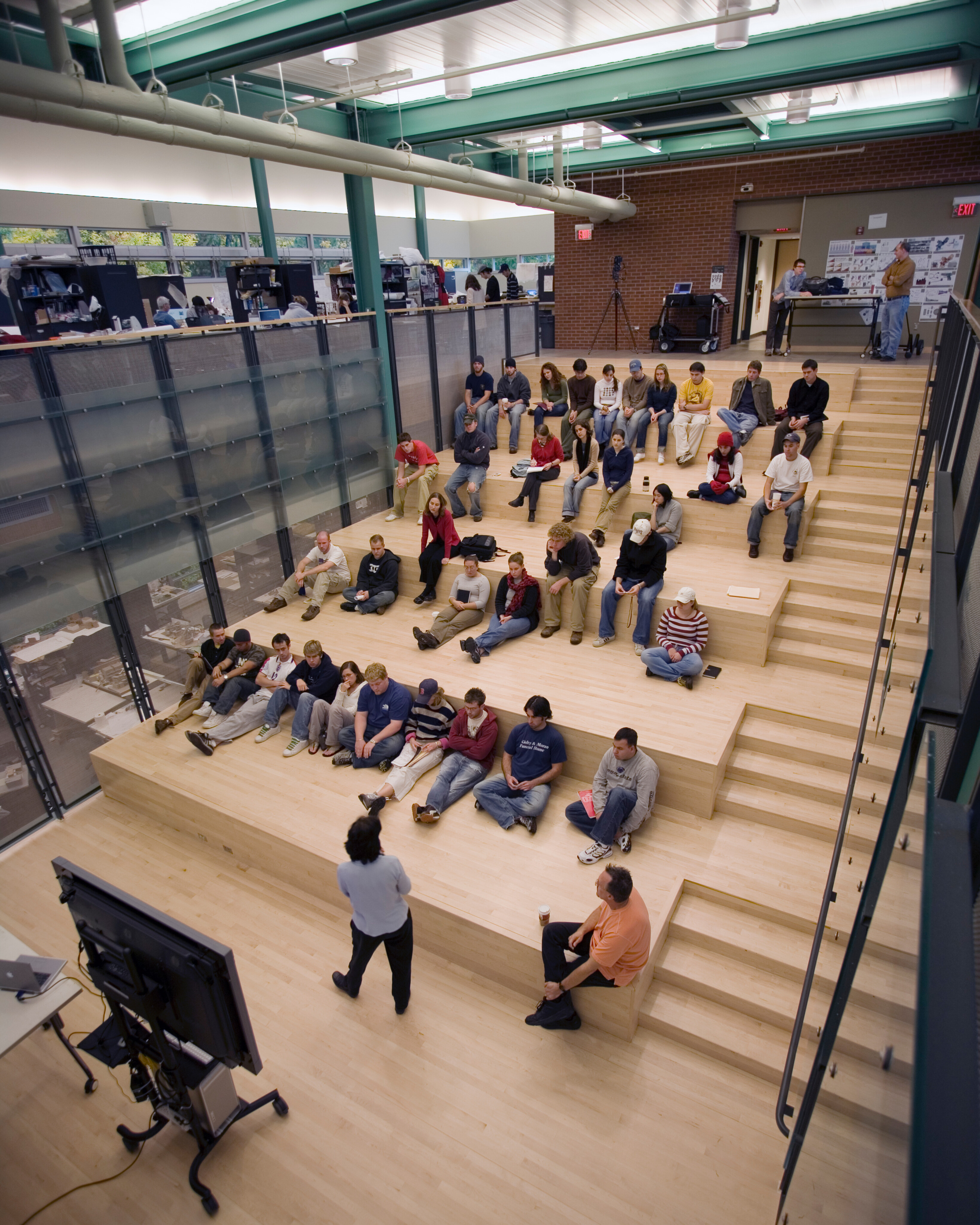 A group of people seated on tiered wooden steps facing a presenter in a modern, open space with large windows and industrial-style architecture—a perfect setting reminiscent of Penn State's innovative SOA design.