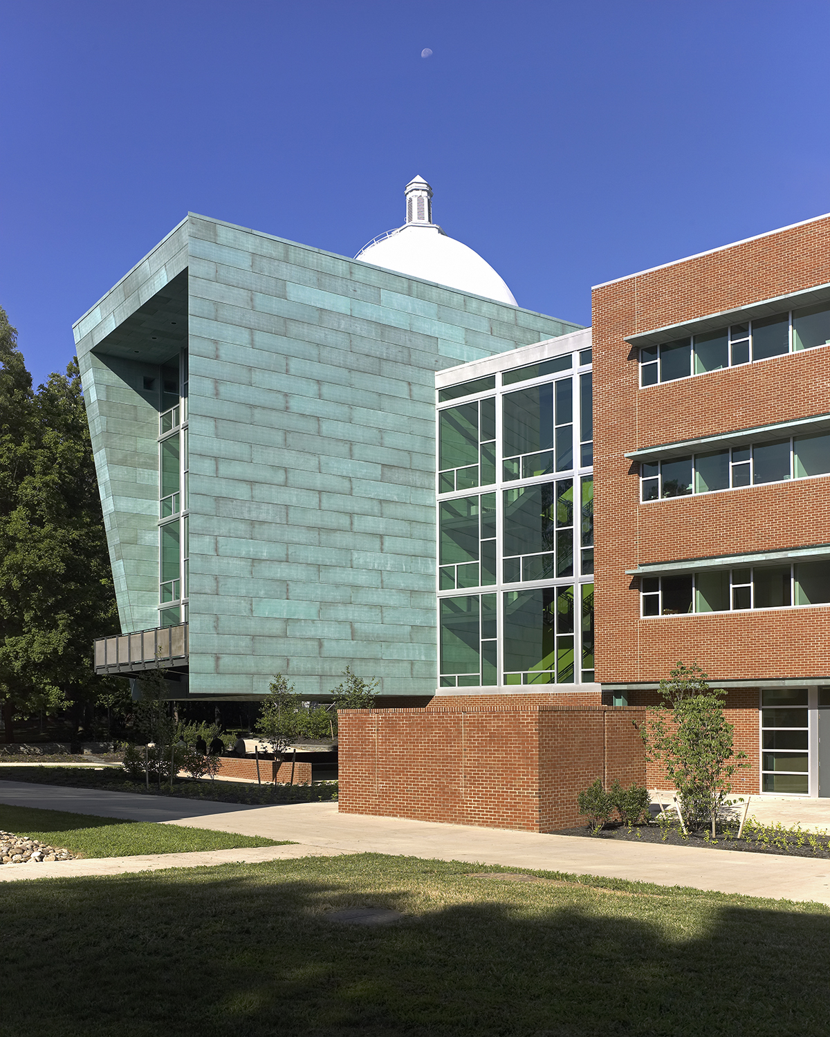 A modern building with glass windows and a distinctive green facade next to a brick structure under a clear blue sky, exemplifying the architectural ingenuity of Penn State SOA.