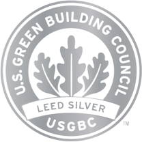 A circular silver emblem with the text "U.S. Green Building Council" and "LEED Silver" around an oak leaf symbol, representing a LEED Silver certification by the USGBC, proudly displayed at The Bridge Homeless Recovery Center.