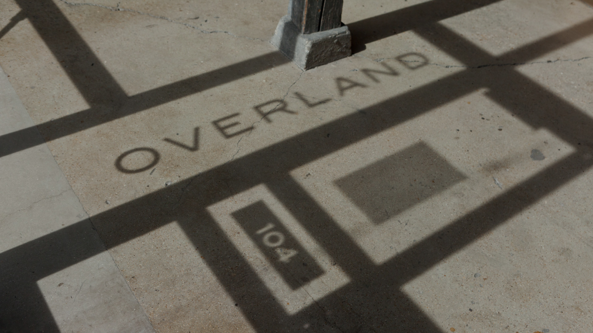 The shadow of a metal structure perfectly casts the word "OVERLAND" and the number "104" on the ground, creating an intriguing display for those who practice mindfulness.