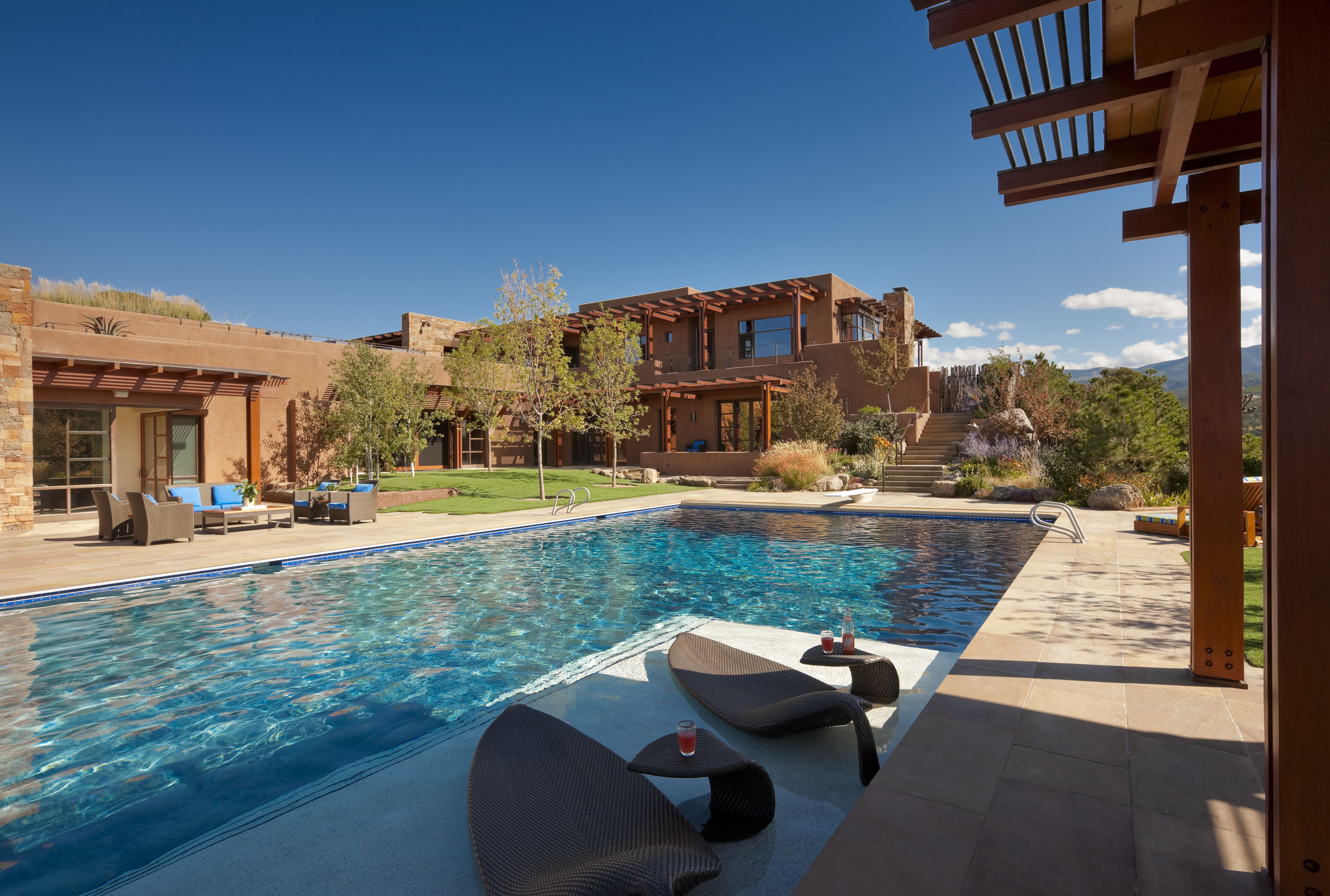 A luxurious Santa Fe retreat with a spacious backyard featuring a large pool, patio seating, and a landscaped garden under clear blue skies.