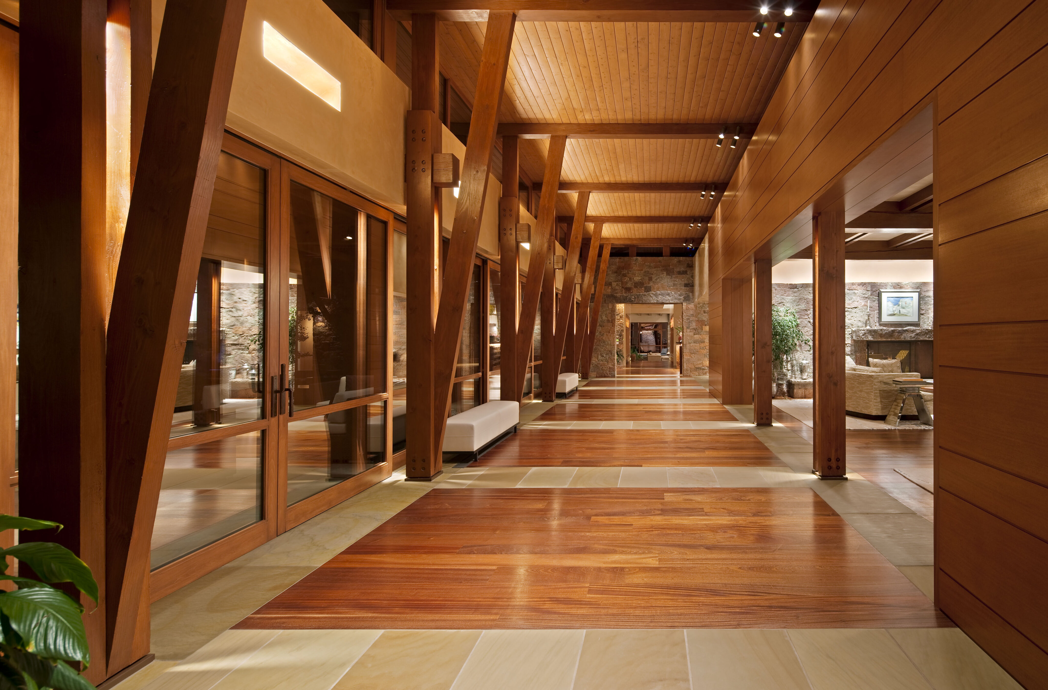 A spacious hallway with wooden beams, polished wood floors, and large glass doors leads to a well-lit room exuding the charm of a Santa Fe Retreat.