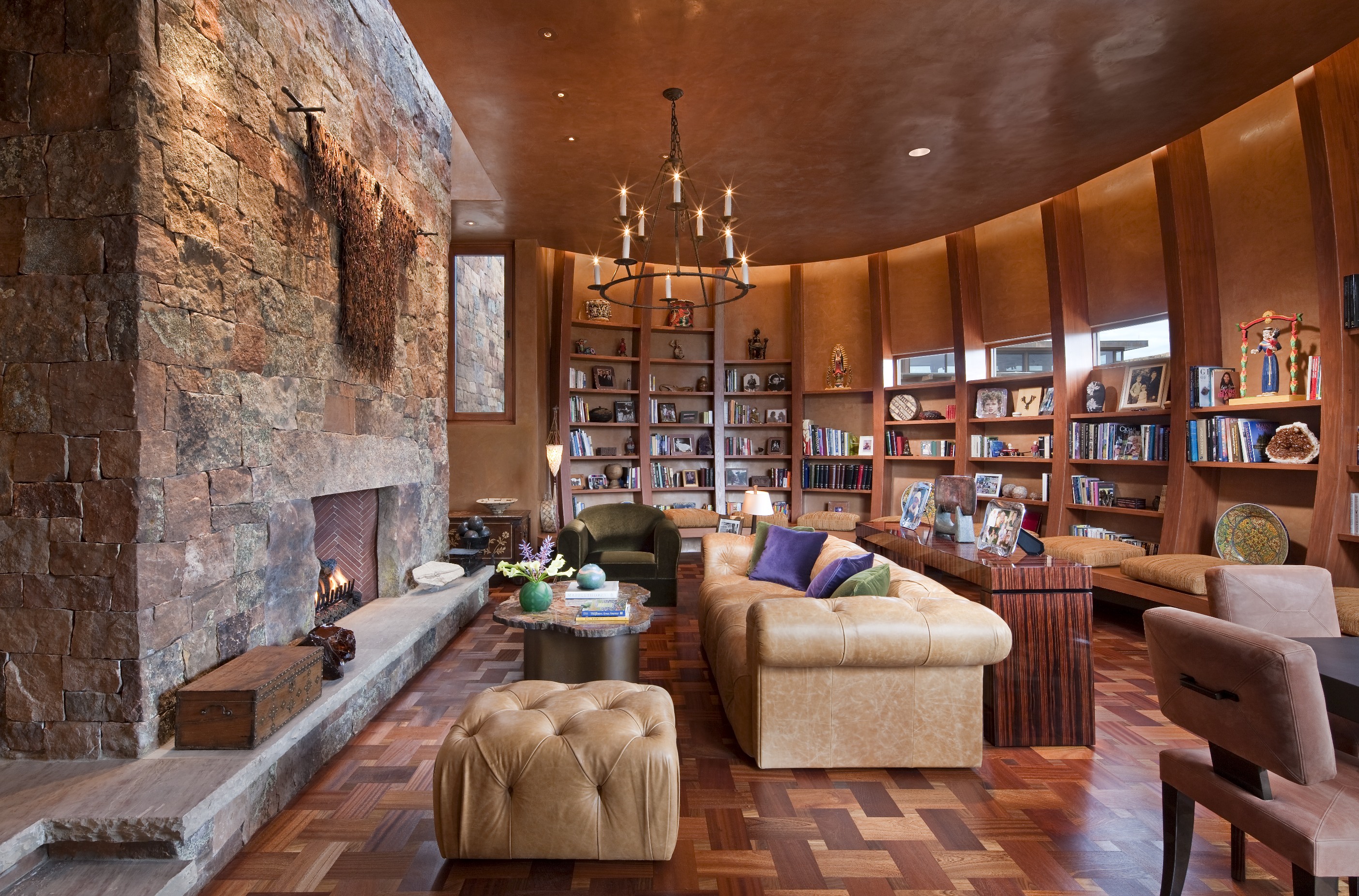 A cozy Santa Fe living room with a stone fireplace, leather furniture, a wooden floor, and a wall of bookshelves decorated with books and personal items creates the perfect retreat.