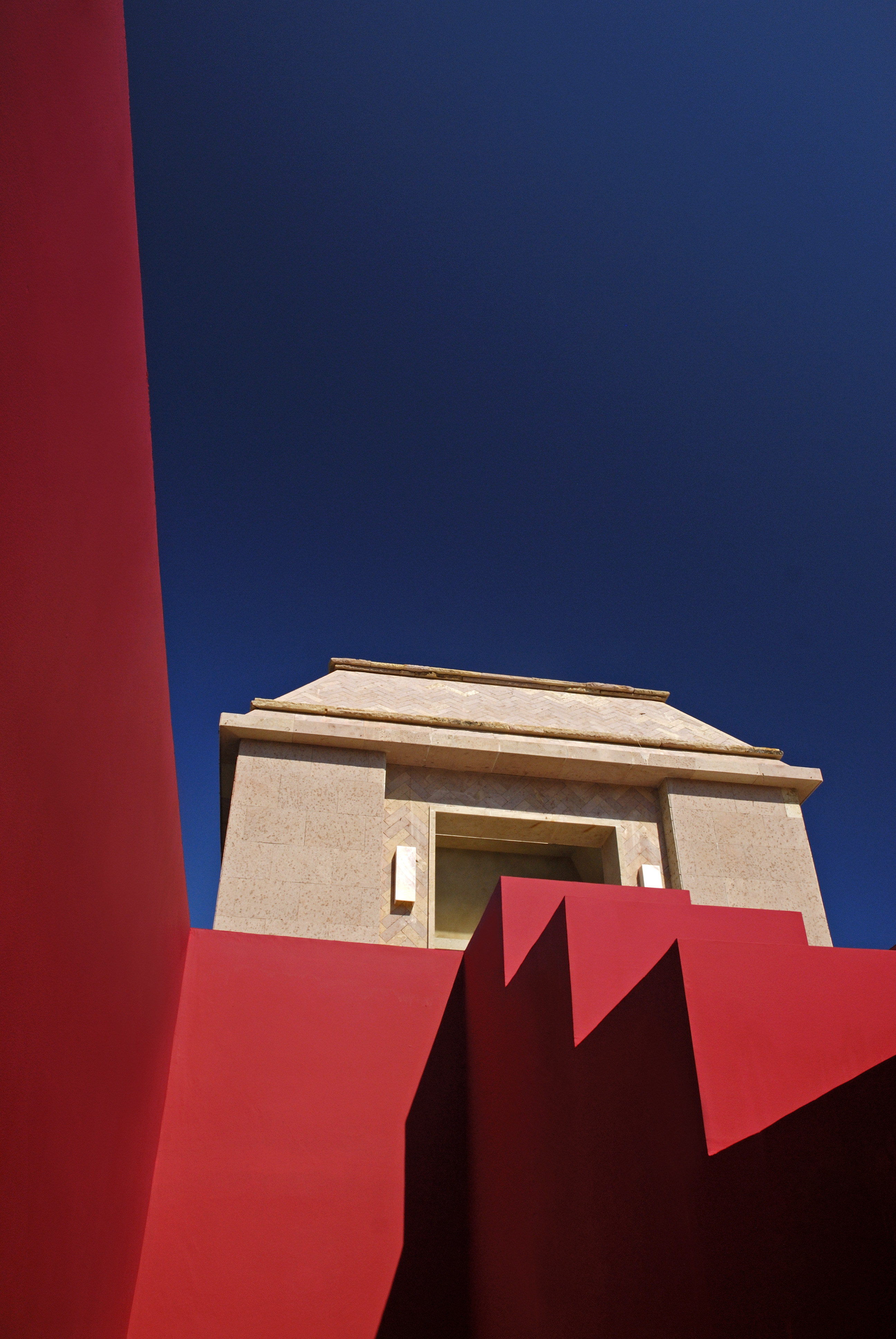 Geometric modern building with red walls and beige upper level set against a deep blue sky, evoking the luxury of Imanta Resort's serene spa.