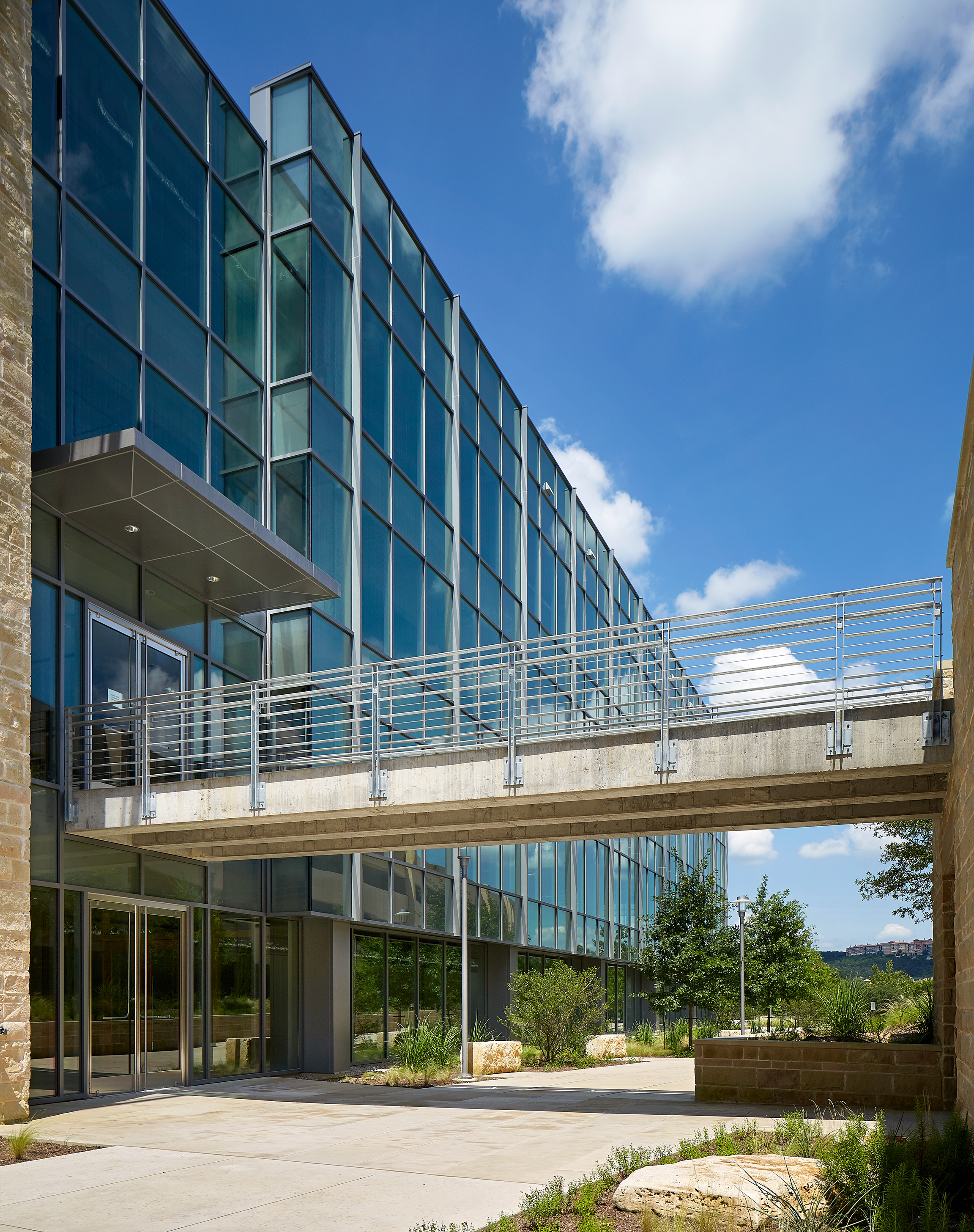 Modern glass building with a pedestrian skybridge connecting two structures. The clear blue sky and greenery complement the architectural design, reflecting an auto-draft precision in its impeccable construction.