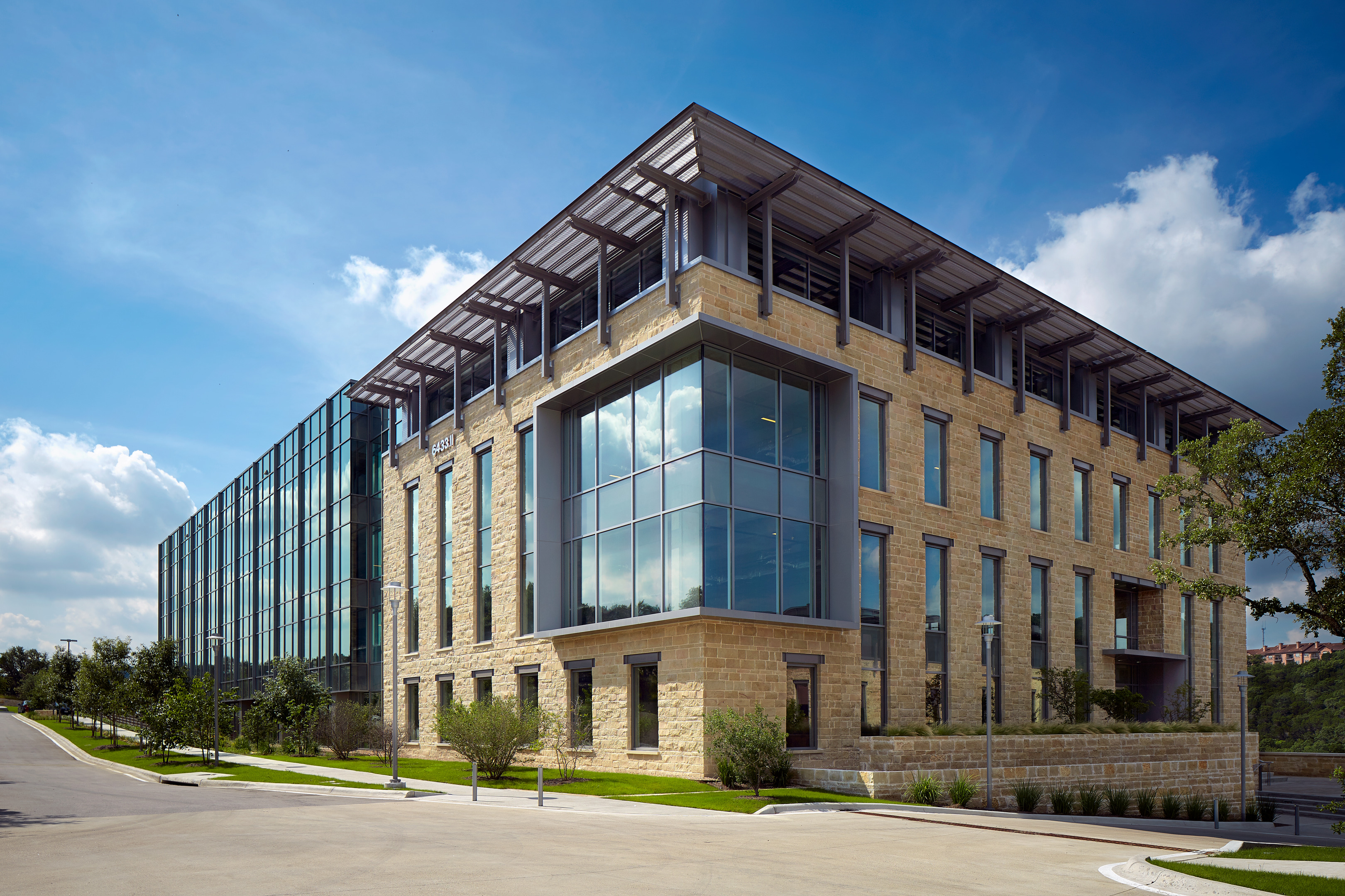 Modern, multi-story building with large glass windows and stone facade, located on a street with a few trees and a clear blue sky background. The design feels like an auto draft of contemporary architecture.