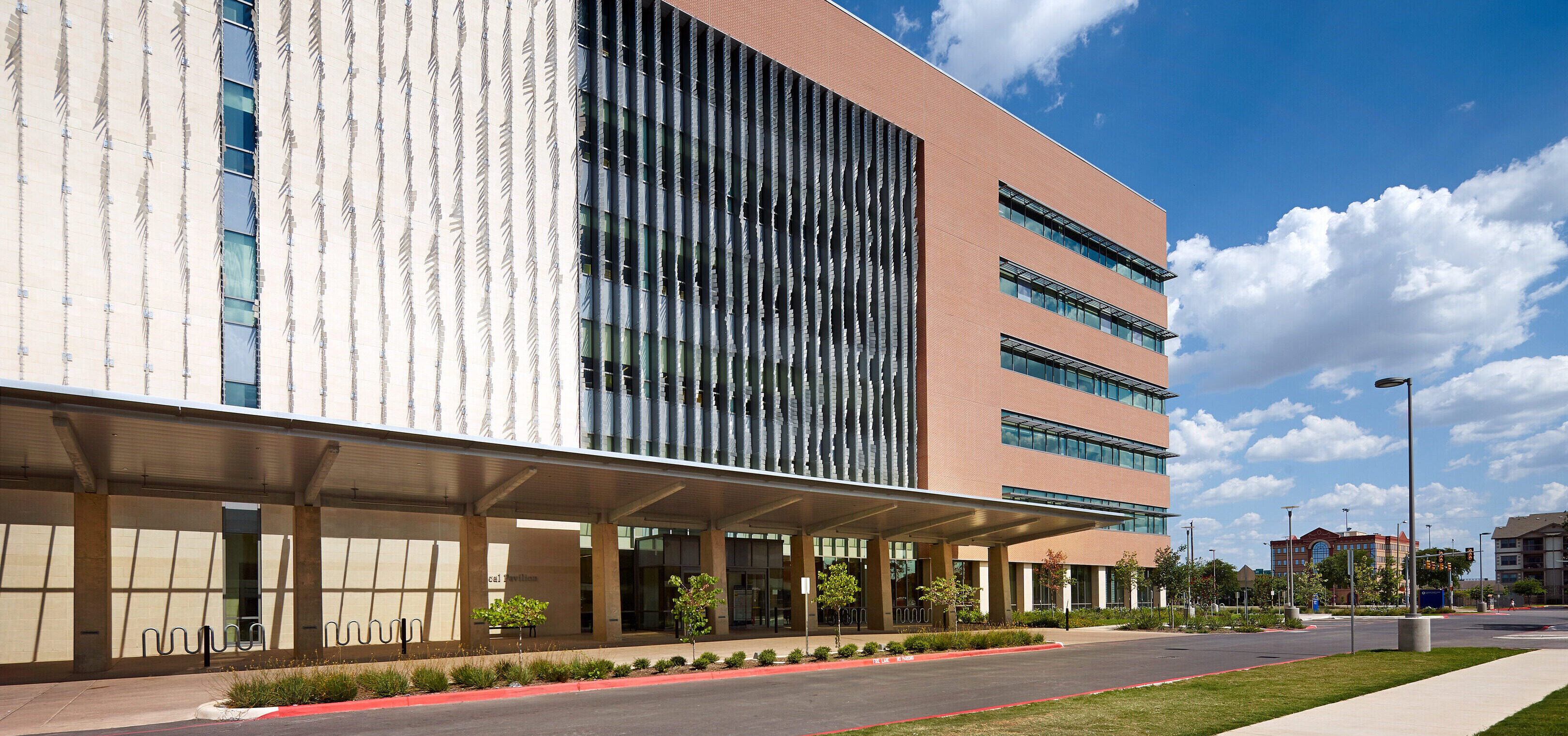 The Robert B. Green Building, part of the University Health System, is a modern multi-story structure with a mix of glass and brick facade. It stands under a partly cloudy sky, featuring a covered entrance and surrounded by lush greenery.