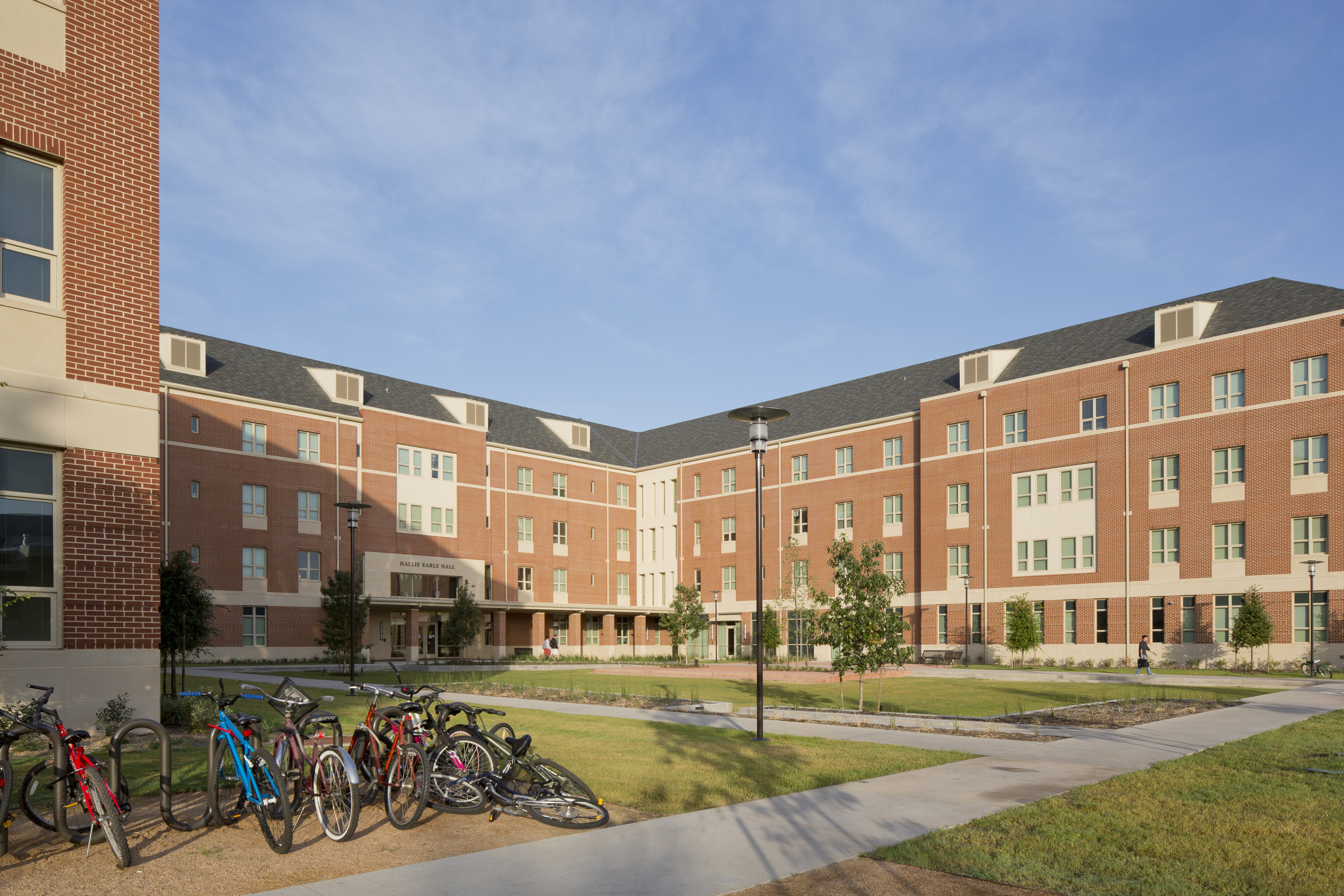 A large brick-and-beige building surrounds a grassy courtyard, with several bicycles parked on a rack in the foreground, reflecting the Master Plan of Baylor University.