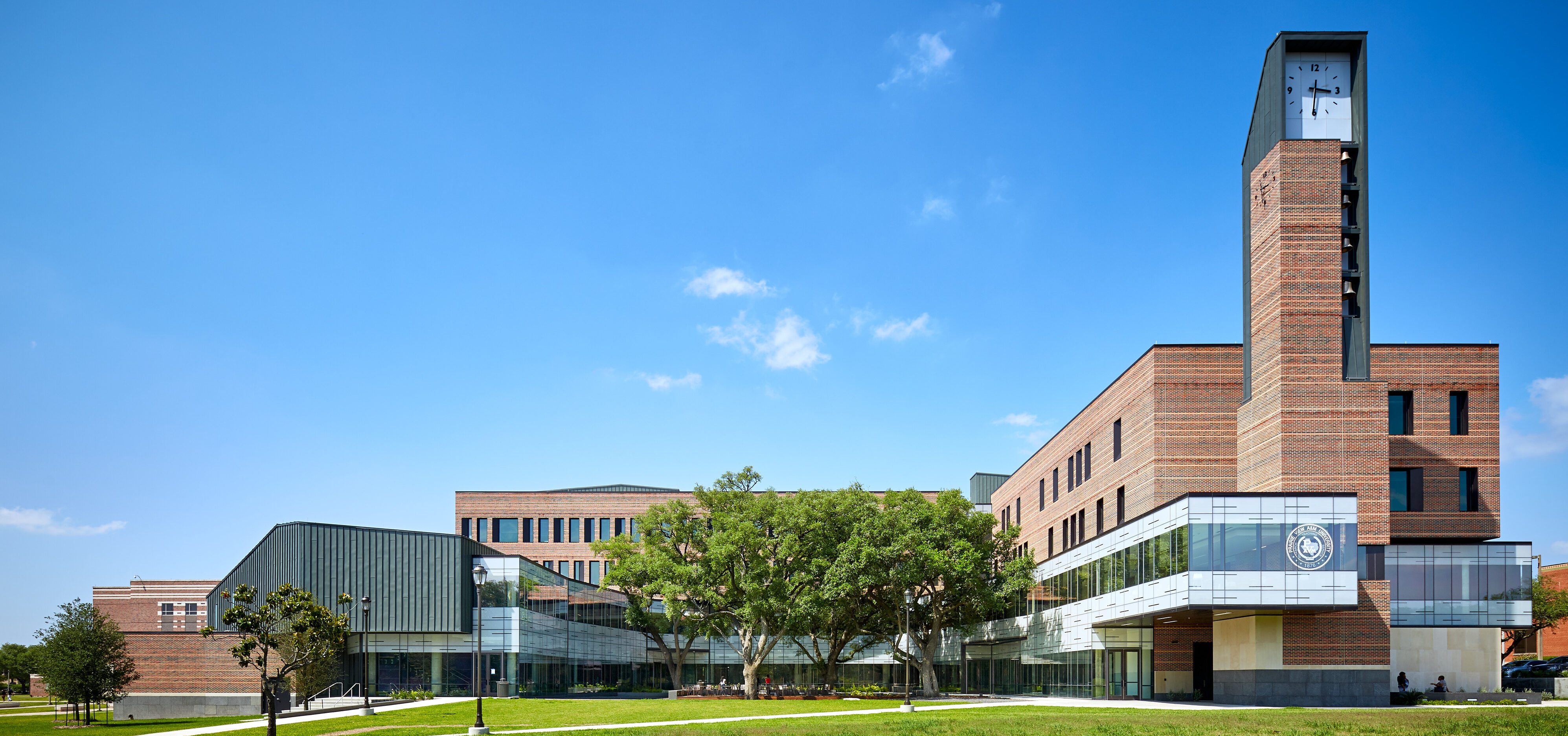 A modern brick and glass university building with a clock tower, surrounded by green lawns and trees under a clear blue sky, stands proud at Prairie View A&M.