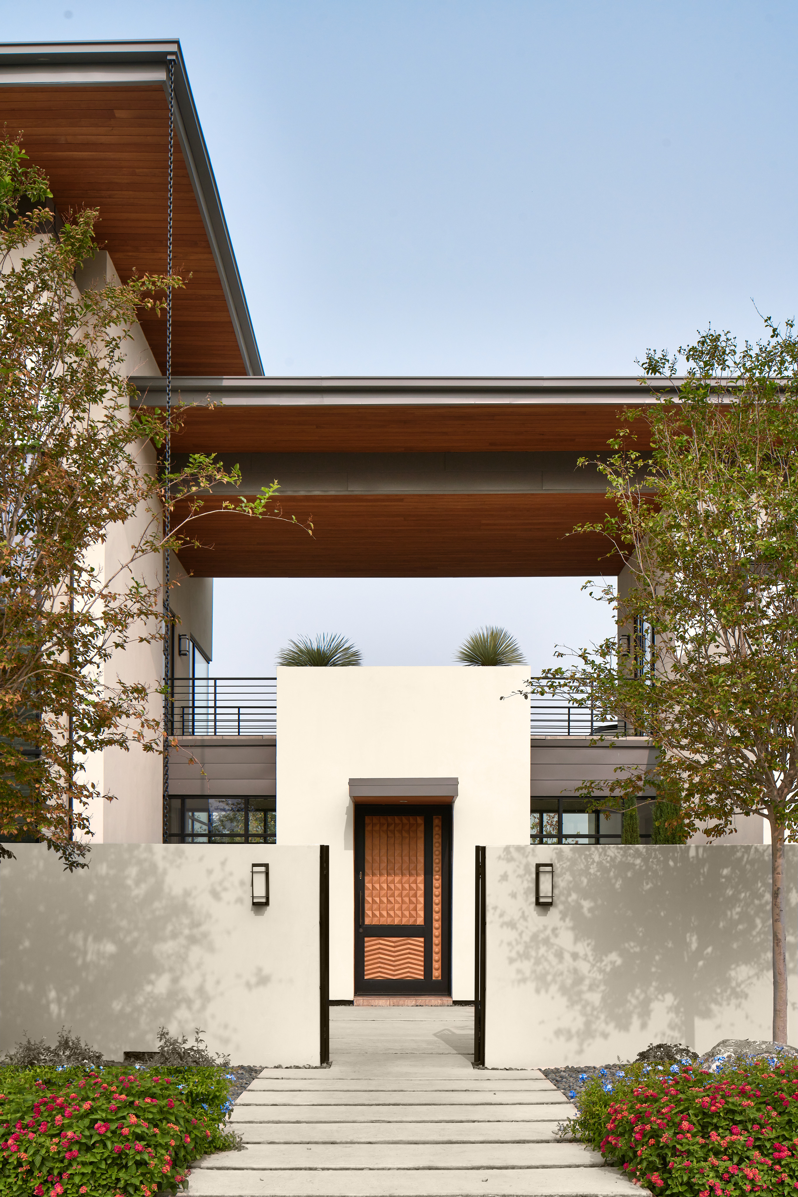 Modern two-story Midland Residence with a minimalist design, featuring a white exterior, wooden accents, a central entrance door, and a landscaped front yard with trees and flowers.