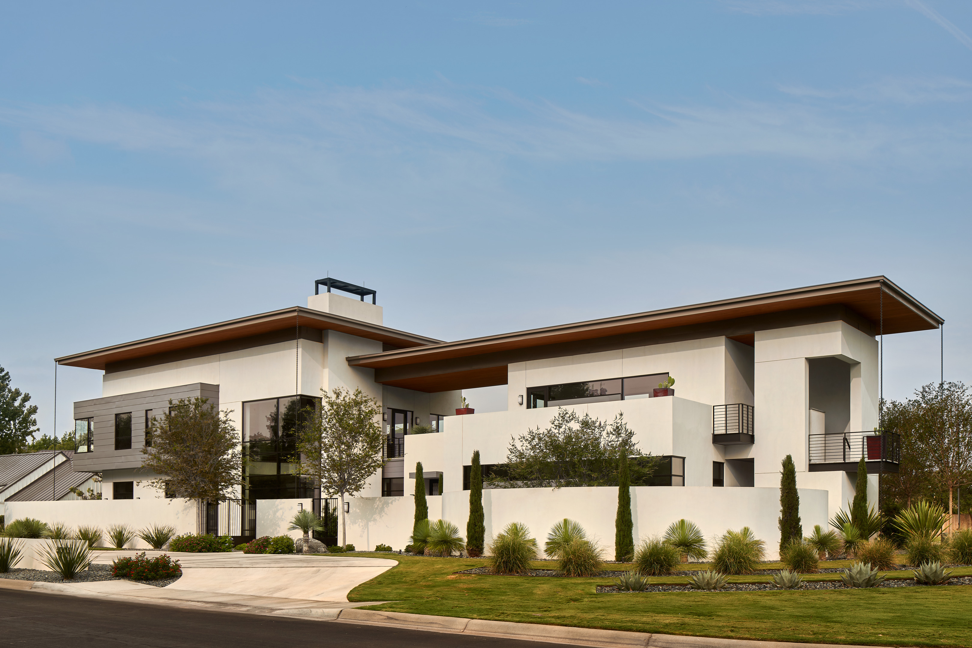 The Midland Residence is a modern, multi-story house with a flat roof, large windows, and balconies, surrounded by a landscaped garden with various plants and a manicured lawn.