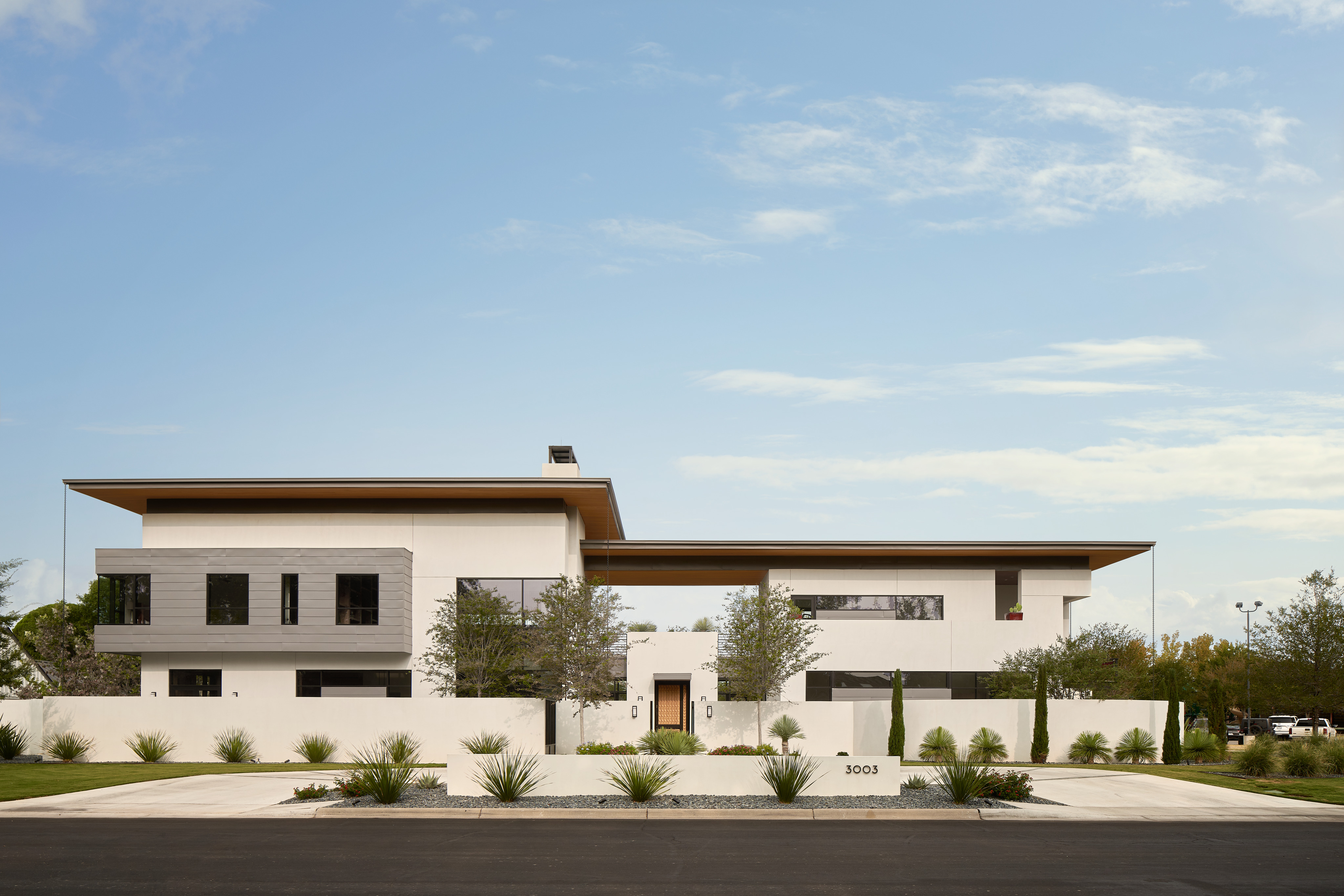 The Midland Residence is a modern, two-story house with clean lines and large windows, set in a landscaped yard with desert plants and a smooth driveway. The house is painted in white and grey tones.