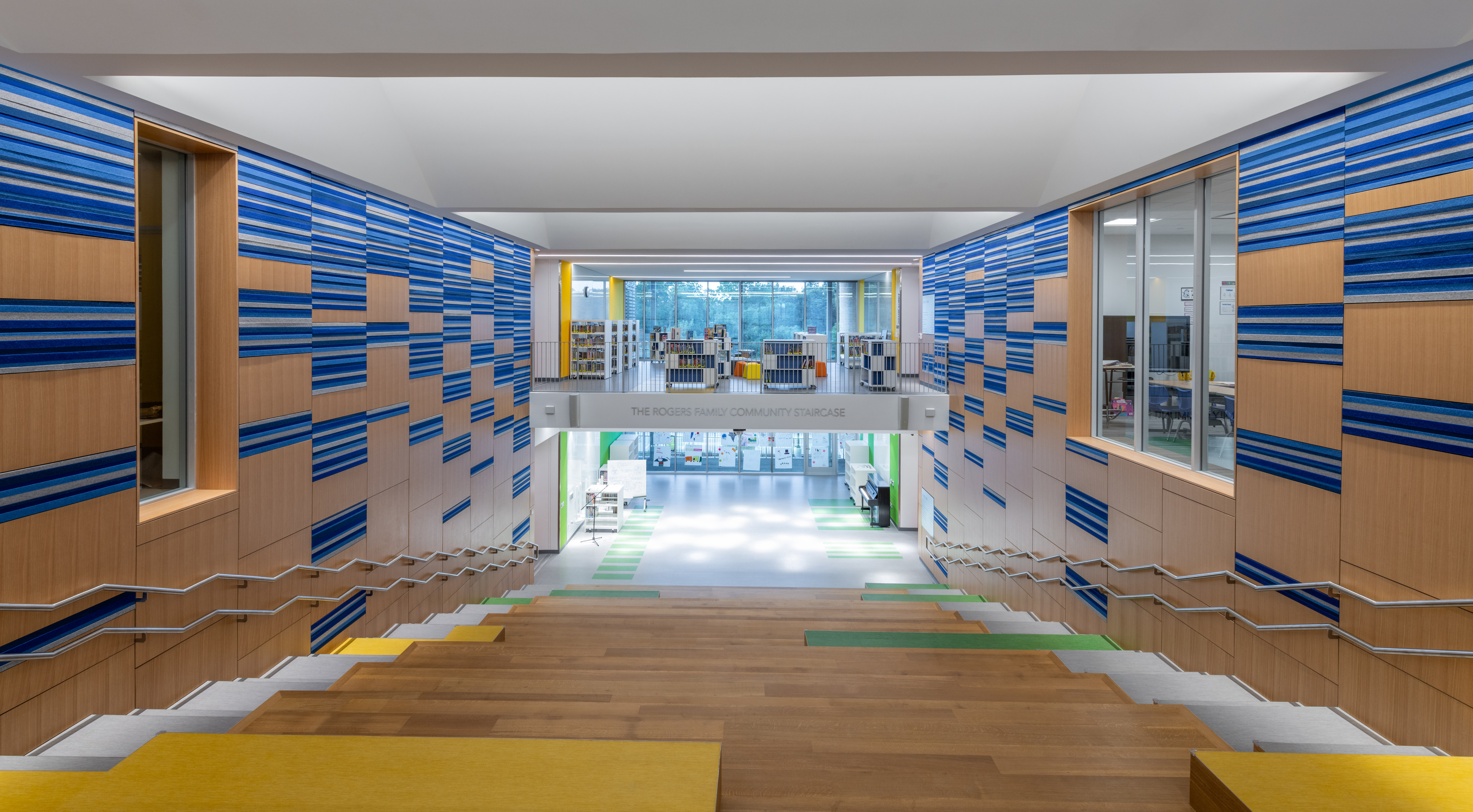 Indoor view of a modern library within the Lower School, featuring colorful wall panels, stairs, and bookshelves in the background.