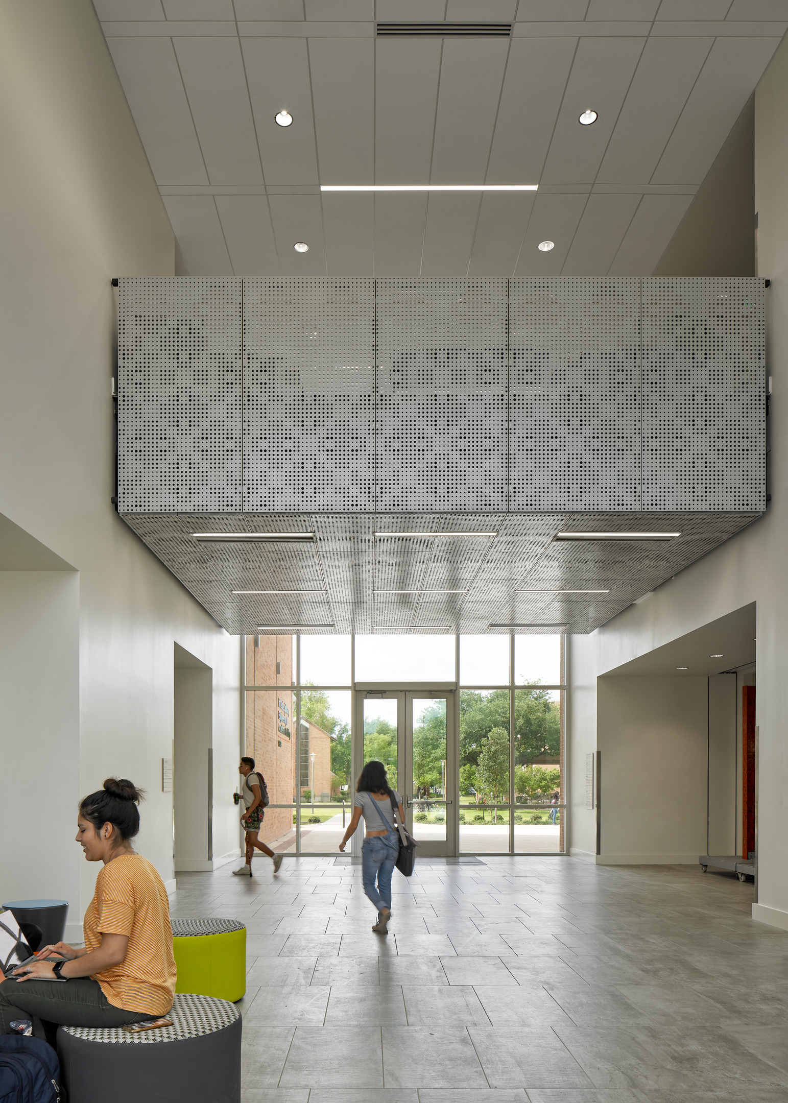 A modern lobby with high ceilings and large windows, featuring students walking and sitting on fashionable furniture.