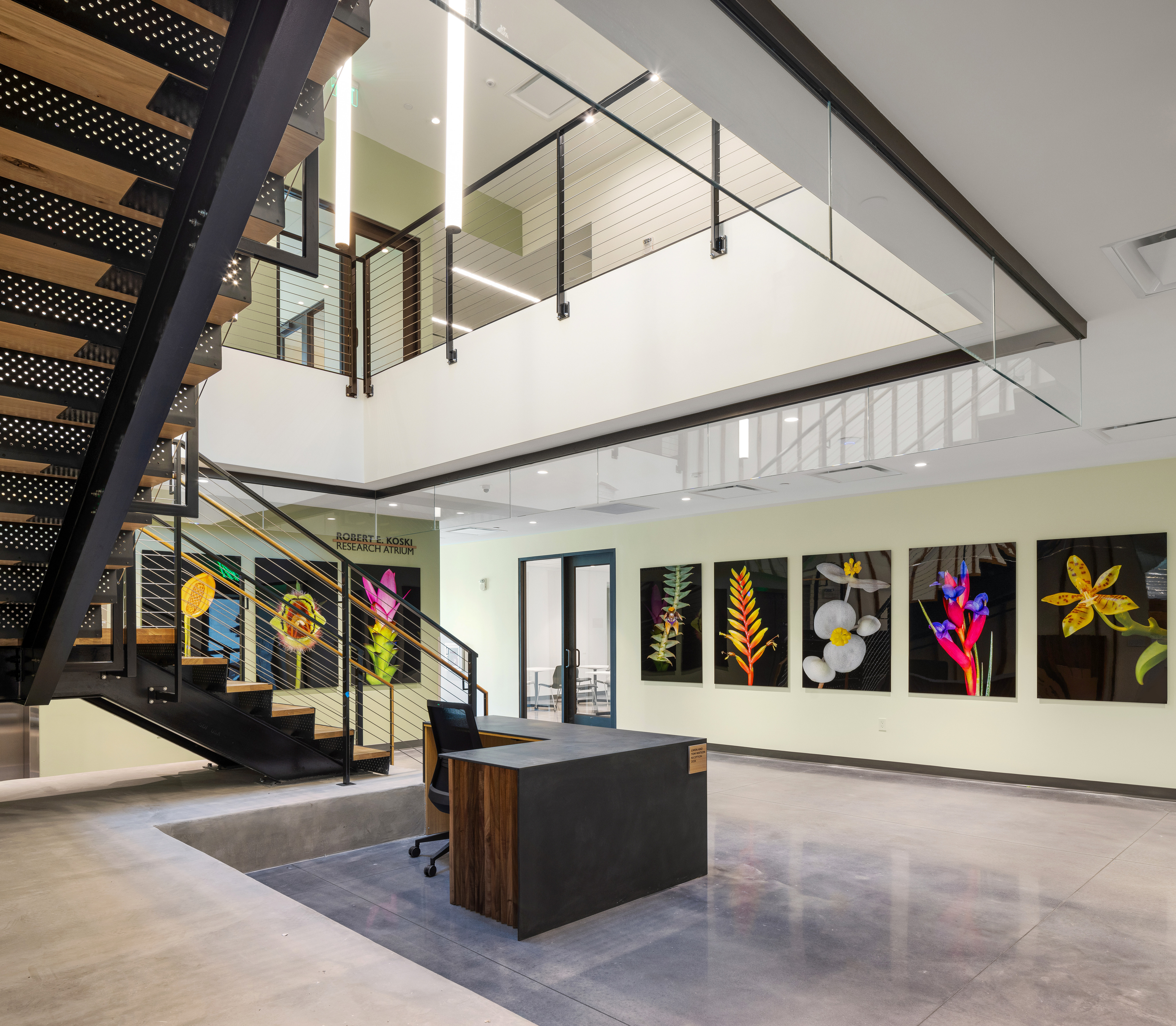 A modern office interior featuring a staircase, glass railings, a reception desk, and vibrant floral artwork on the walls inspired by Marie Selby Botanical Gardens.