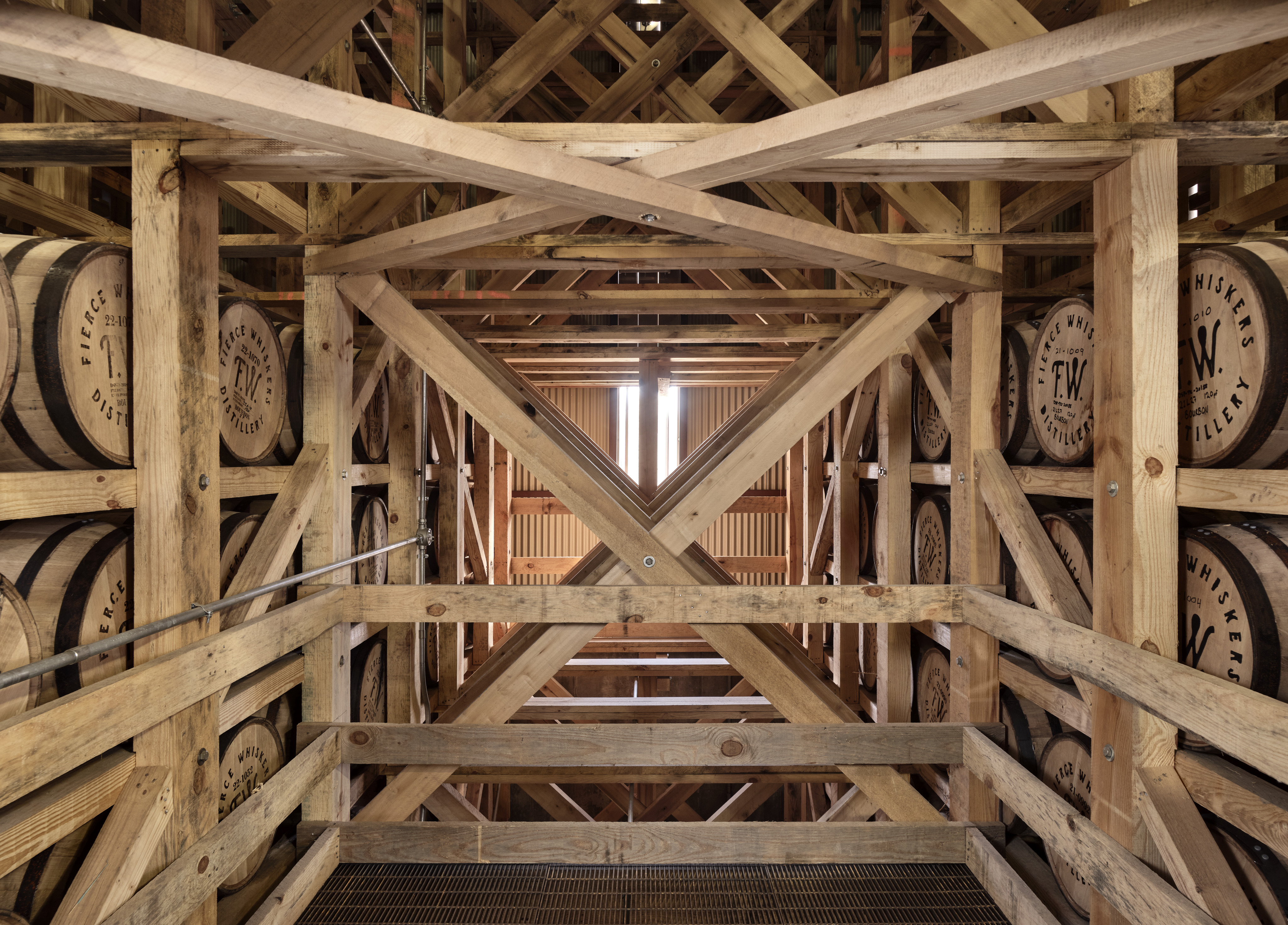 Inside the Distillery, a wooden framework houses stacked whiskey barrels, with natural light filtering in from above, creating an atmosphere that showcases the craftsmanship of Fierce Whiskers.