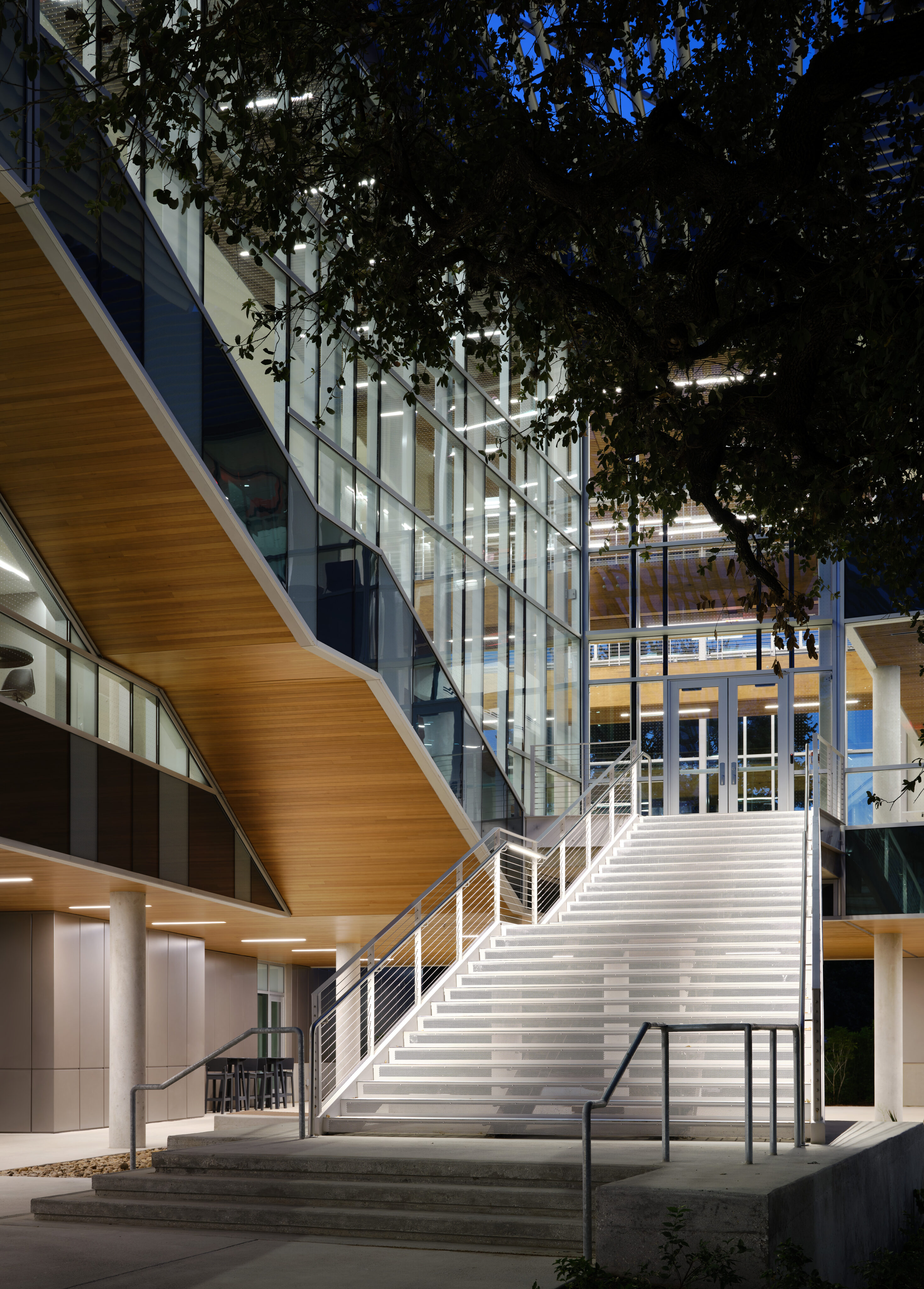 A modern building at Northwest Vista College, with a prominent staircase flanked by glass walls and wood accents, is illuminated at night.