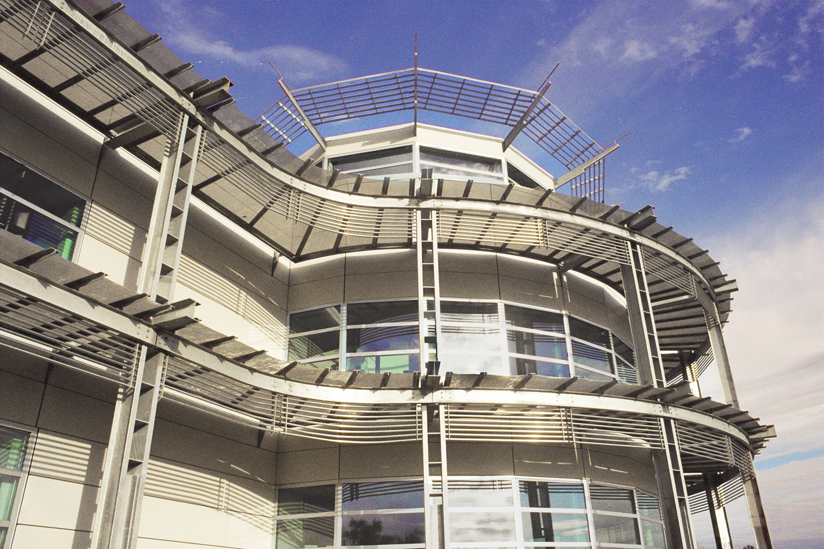 A modern building with curved architectural features and metal accents houses the South Texas Blood & Tissue Center. It has large windows and a multi-tiered design, all set against a partly cloudy sky.