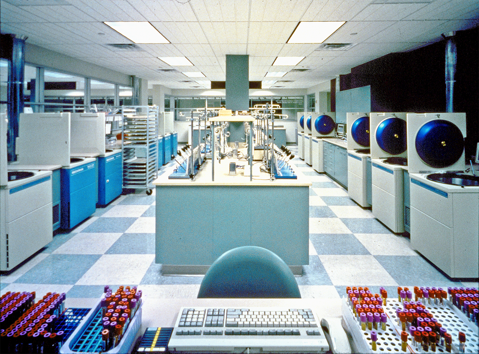 A laboratory interior at the South Texas Blood and Tissue Center features numerous electronic machines, workstations, and test tubes organized neatly in trays on a desk in the foreground.