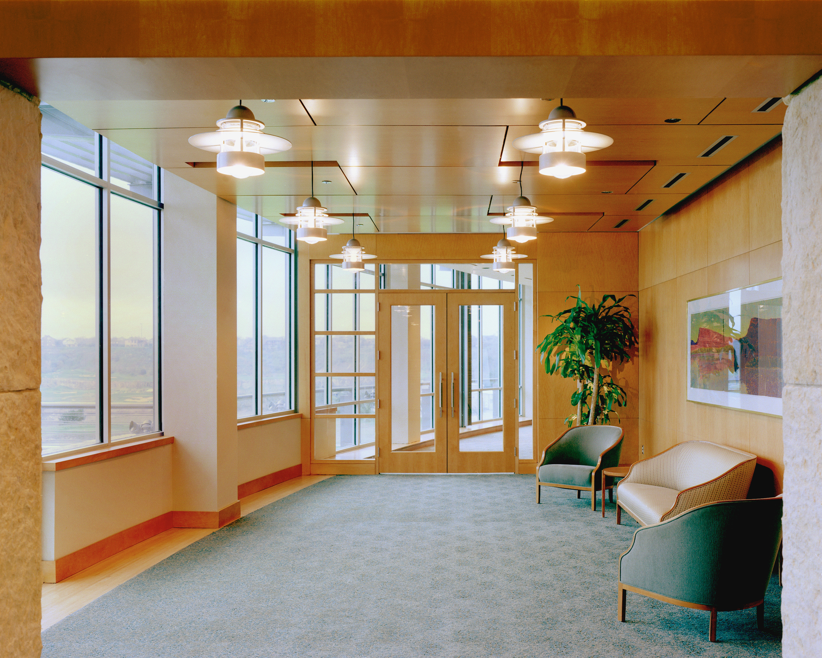 A modern office lobby at Clear Channel's headquarters features large windows, two armchairs, a potted plant, overhead lights, and framed artwork on the wall.