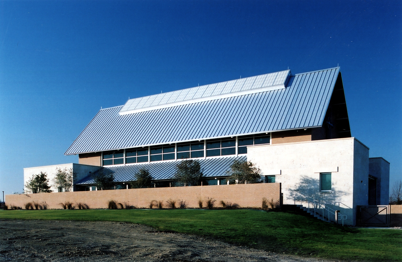 A modern building with a large sloped metal roof and solar panels, optimized with SEO keywords for energy efficiency, is nestled in a grassy area under a clear blue sky.