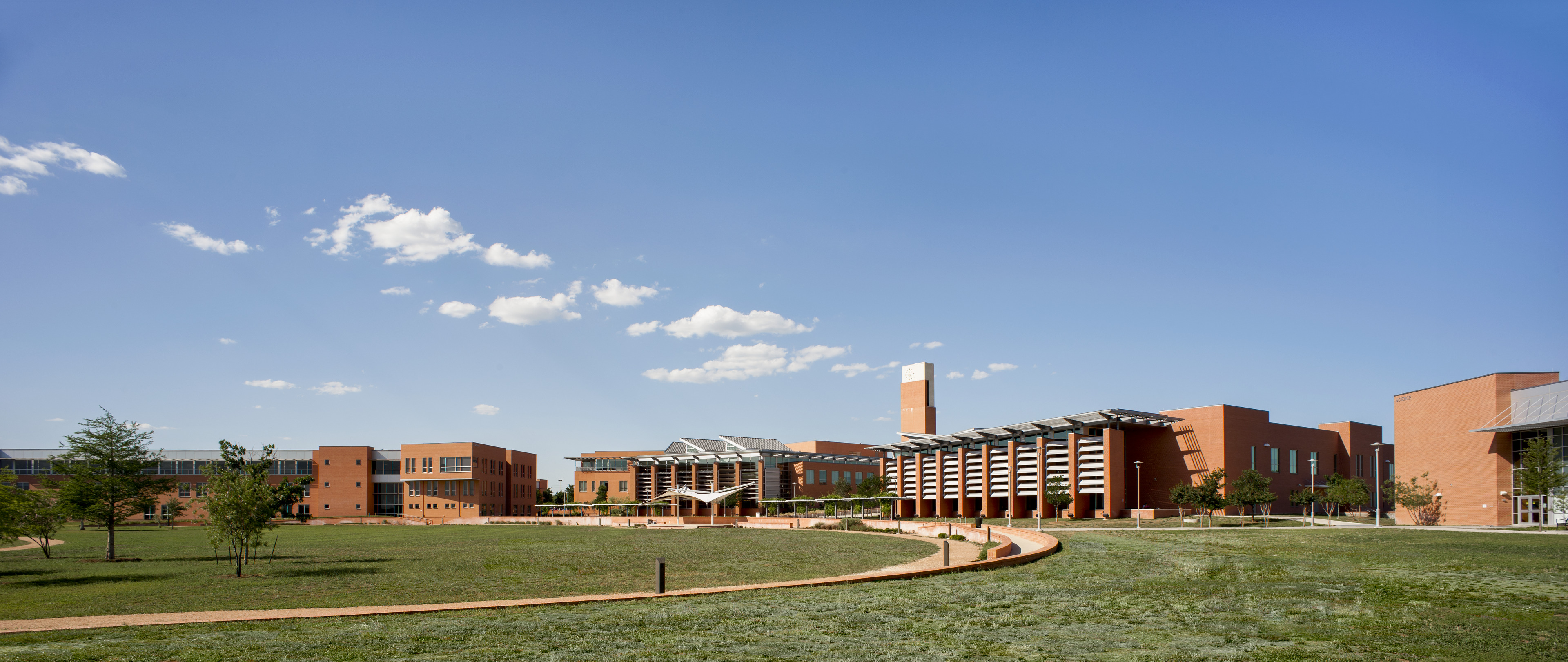 A modern school building with orange brick walls, large windows, and solar panels on the roof stands proudly against a clear blue sky. The grassy foreground features a winding path that seems carefully planned—much like an auto draft sketch brought to life.