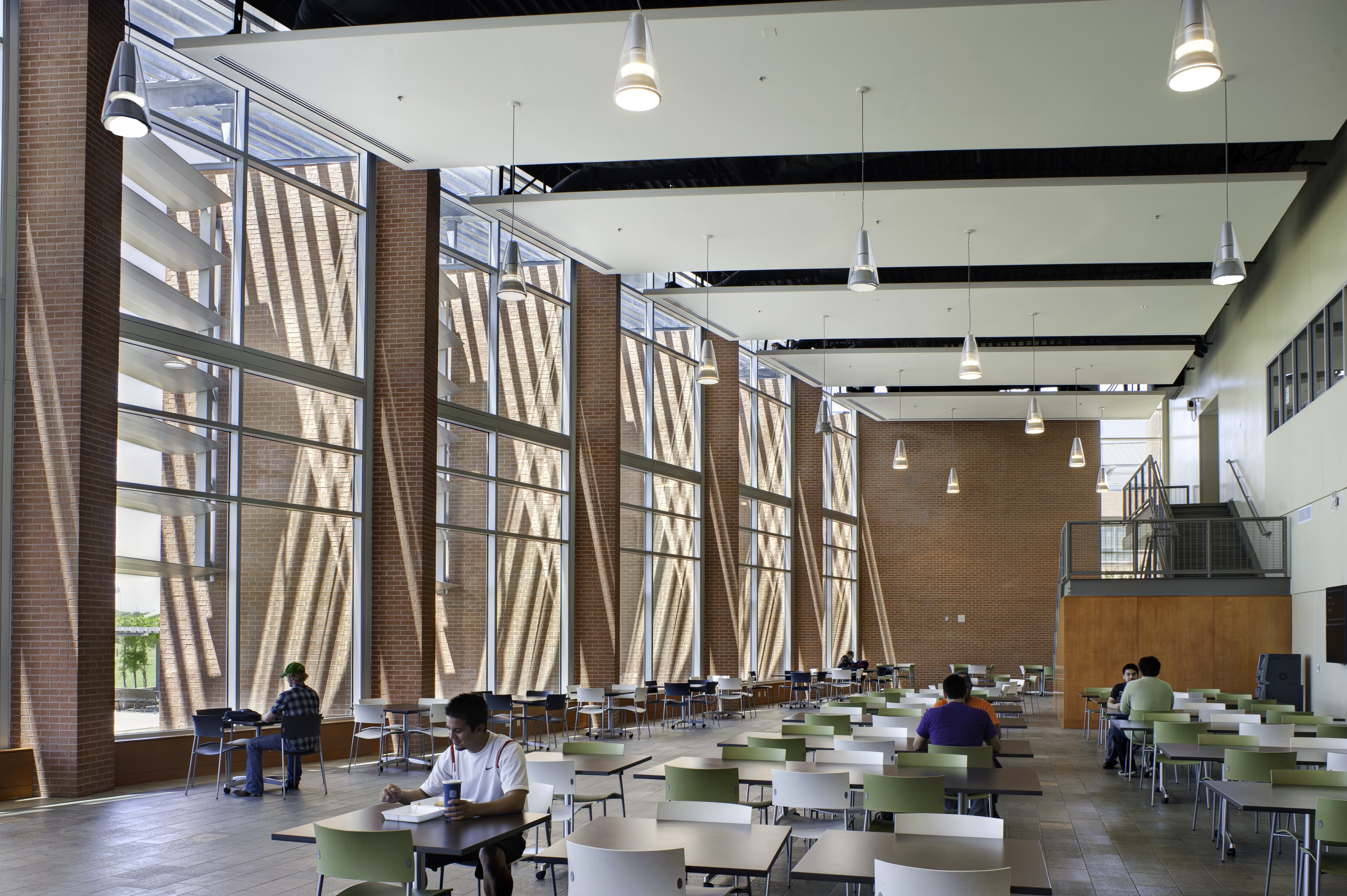 The spacious indoor cafeteria, designed with modern flair and large windows, offers a peaceful ambiance reminiscent of an auto draft—naturally arranging the few people seated at tables into a harmonious scene.