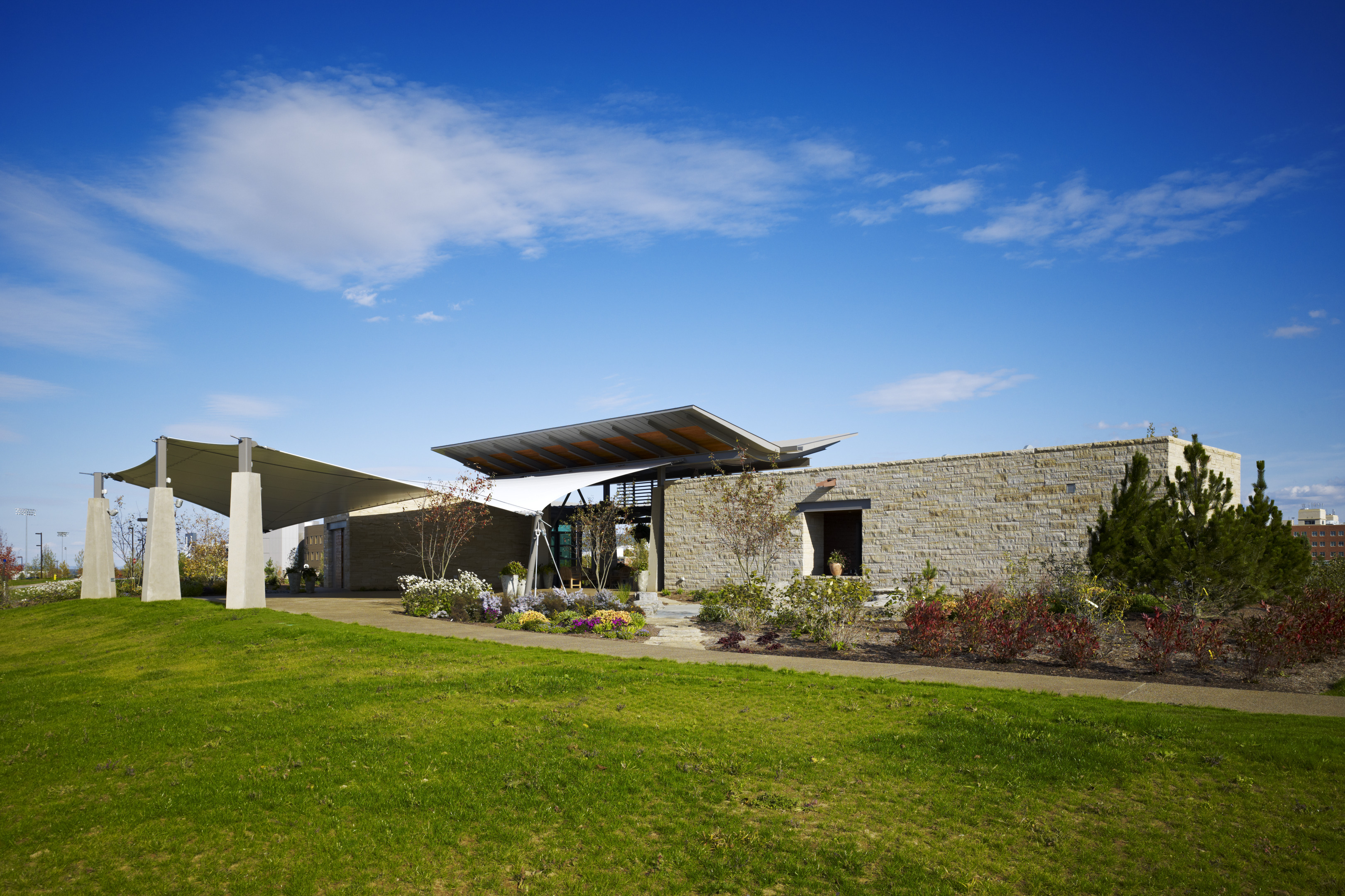 Modern building with stone walls and large canopy roof, surrounded by landscaped greenery under the clear blue sky, creating an auto draft of elegance and innovation.