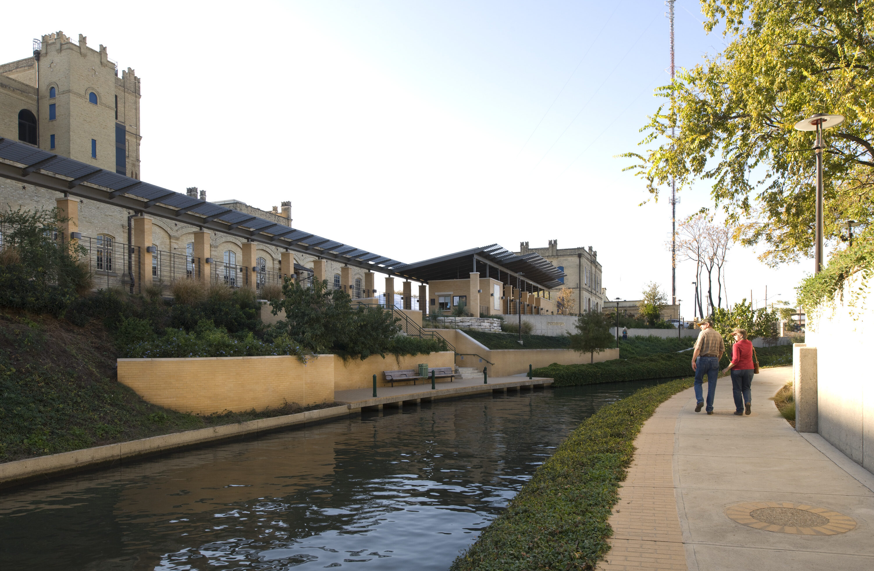 The couple strolls along a riverside path, the gleaming solar panels on the historic building catching their attention. If you have additional details, please provide that for a better analysis of this charming scene's potential.