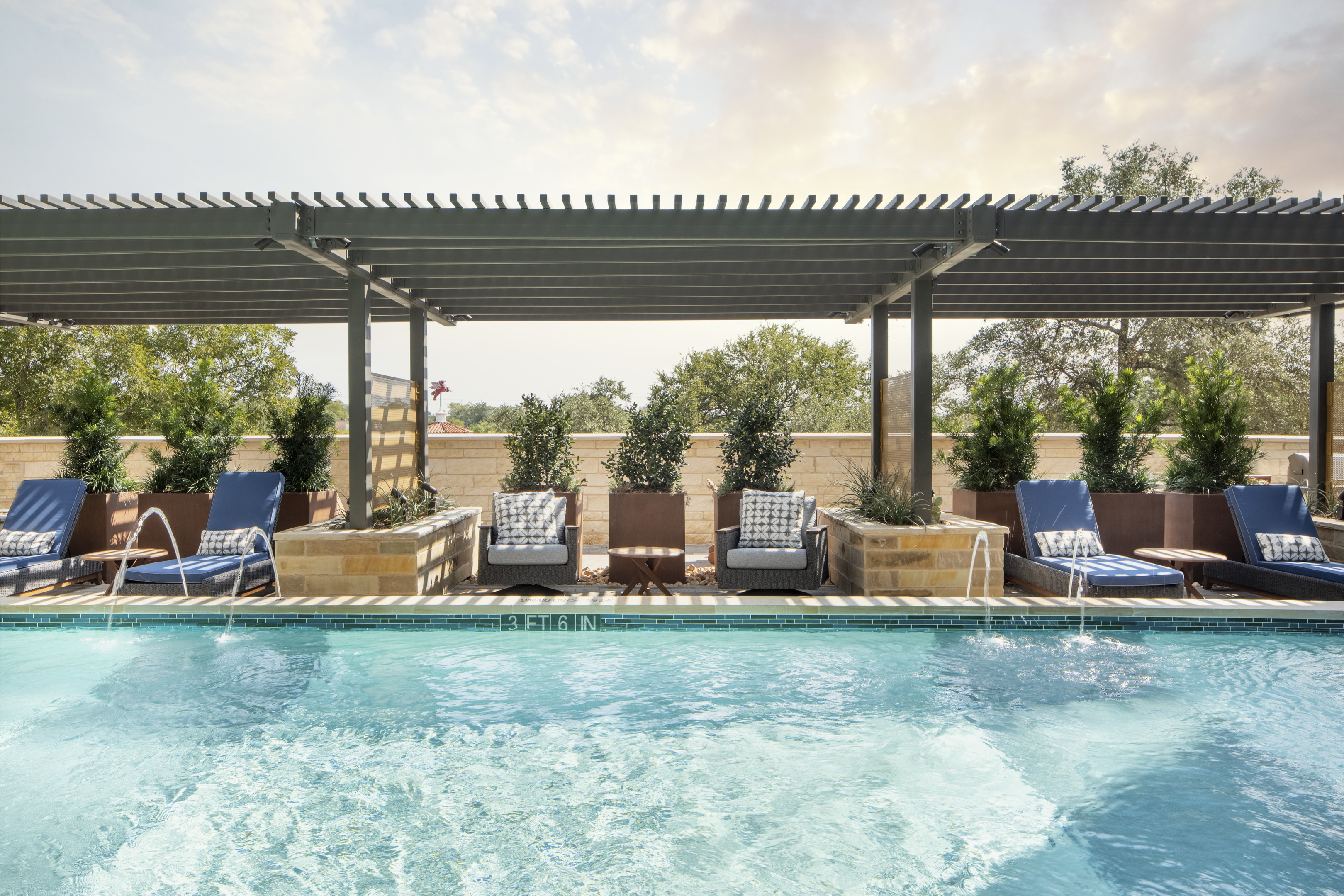 A swimming pool with lounge chairs and plants under a pergola on a sunny day, nestled in the serene environment of Magnolia Heights' mixed-use development.