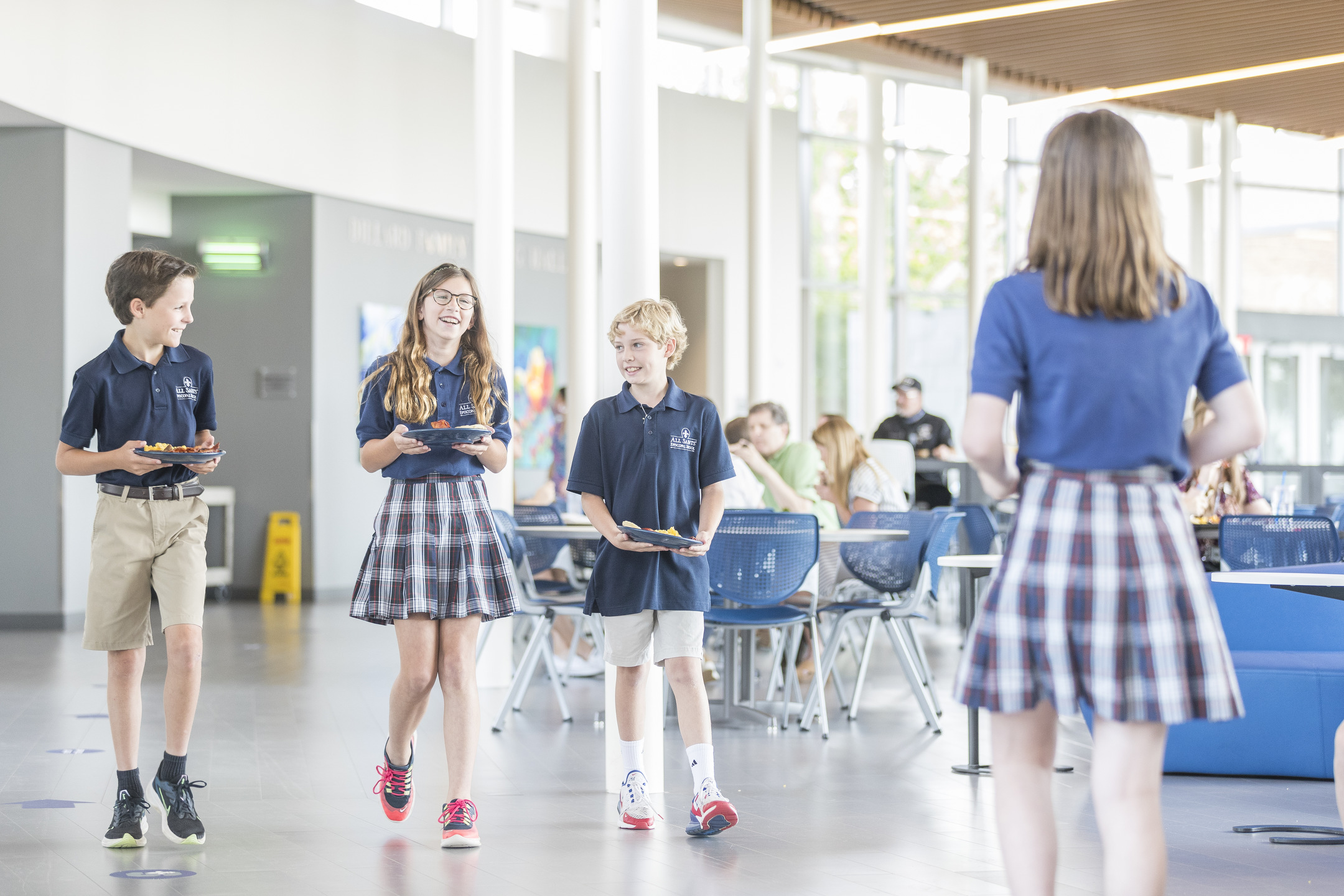 Four students in uniform stroll through the cafeteria, carefully balancing trays as if on auto draft mode.