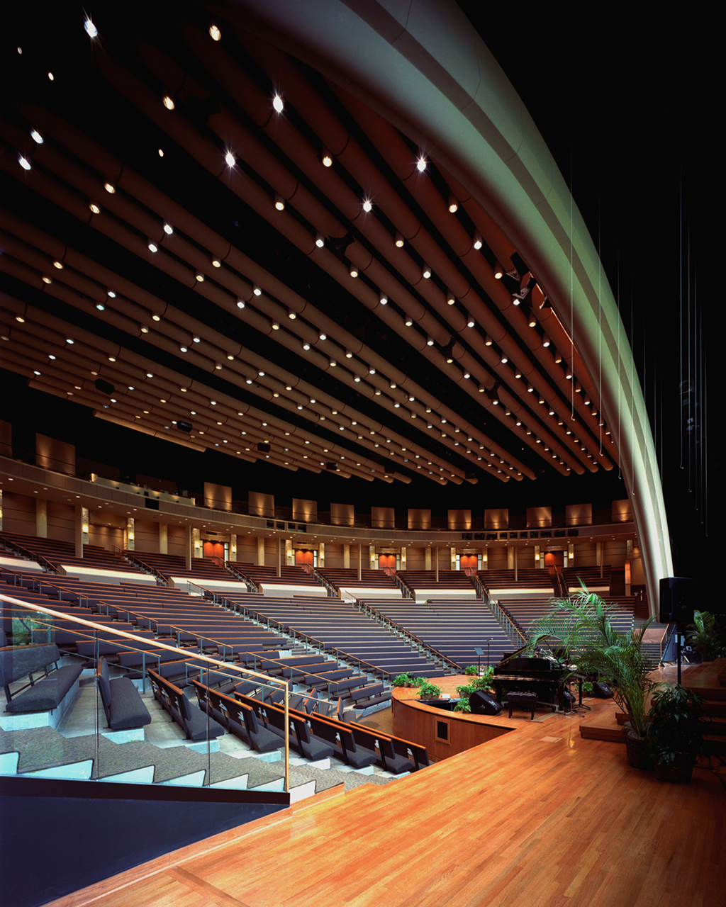 The large, modern auditorium at Riverbend Church offers tiered seating and sleek wooden flooring, with potted plants adding a touch of nature to the stage view.