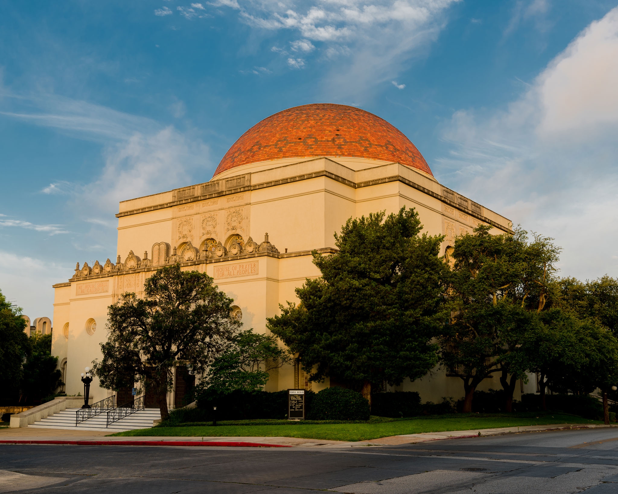 A magnificent beige building with a striking red dome and intricate detailing is nestled among lush trees under a vibrant blue sky, exuding timeless elegance.