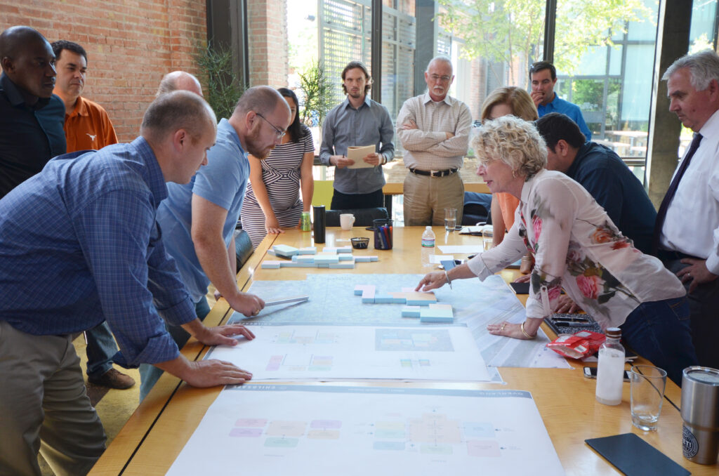 A group of people gather around a table at the Salado Creek campus, examining papers and discussing trauma-informed design strategies.